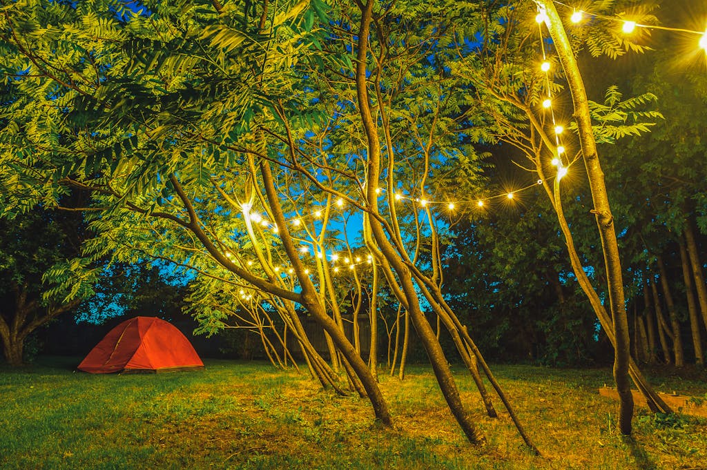 A serene evening campground scene featuring string lights illuminating trees and a tent.