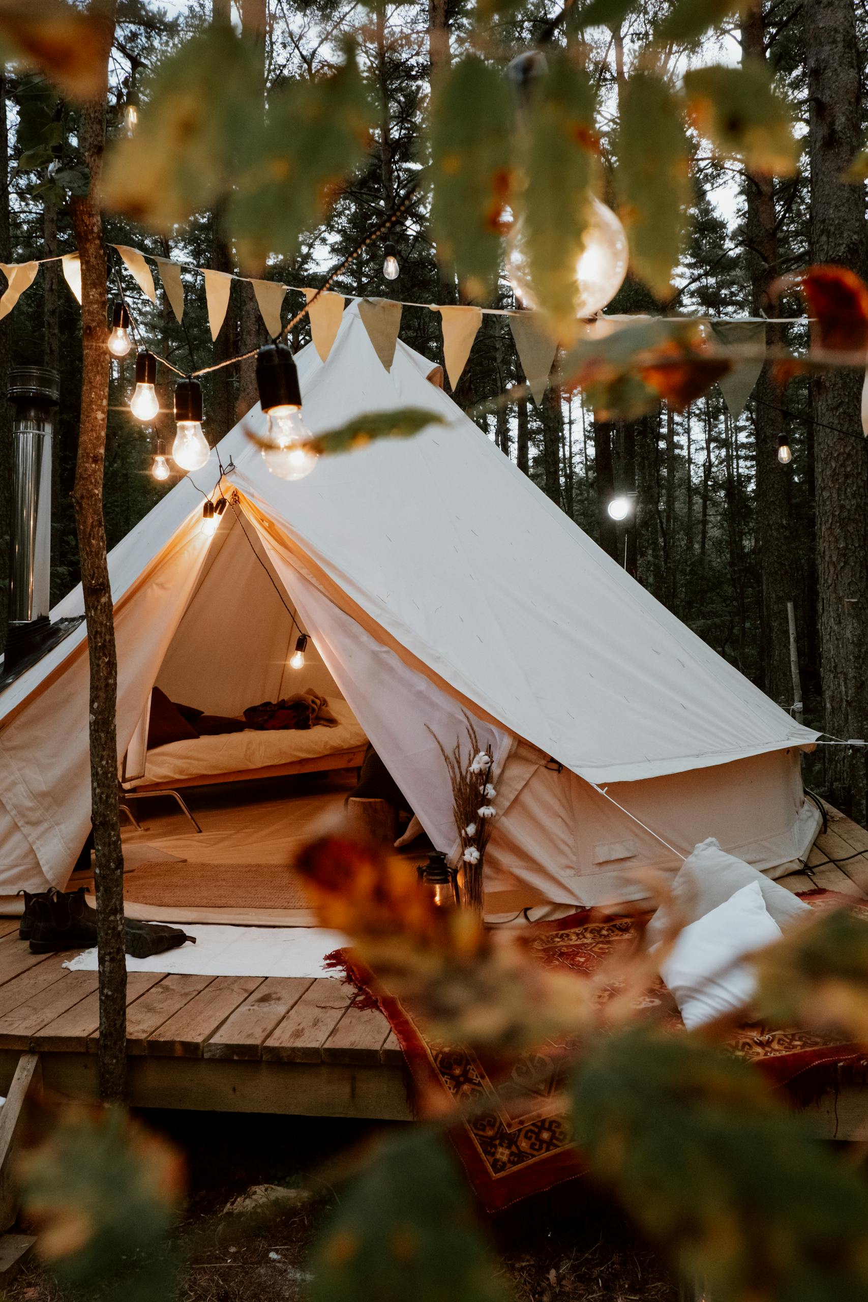 A cozy glamping tent amidst forest trees decorated with warm lights for a relaxing camping experience.