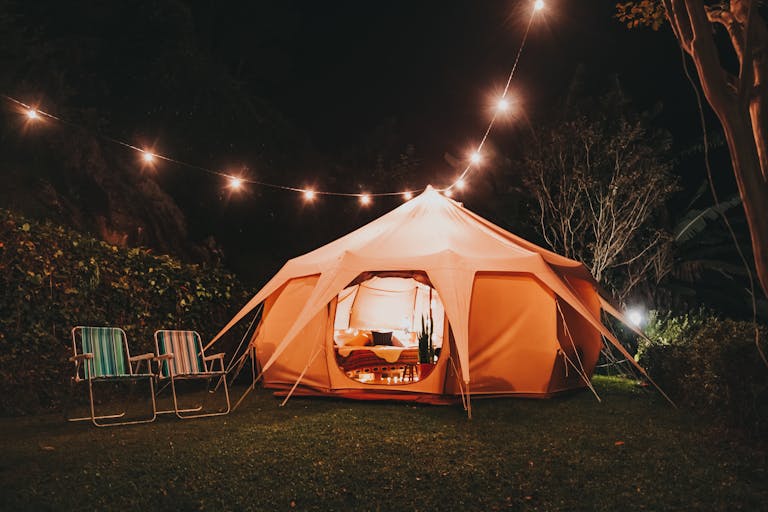 Bell tent glowing at night in a UK back garden with fairy lights strung along a fence, garden glamping staycation setup