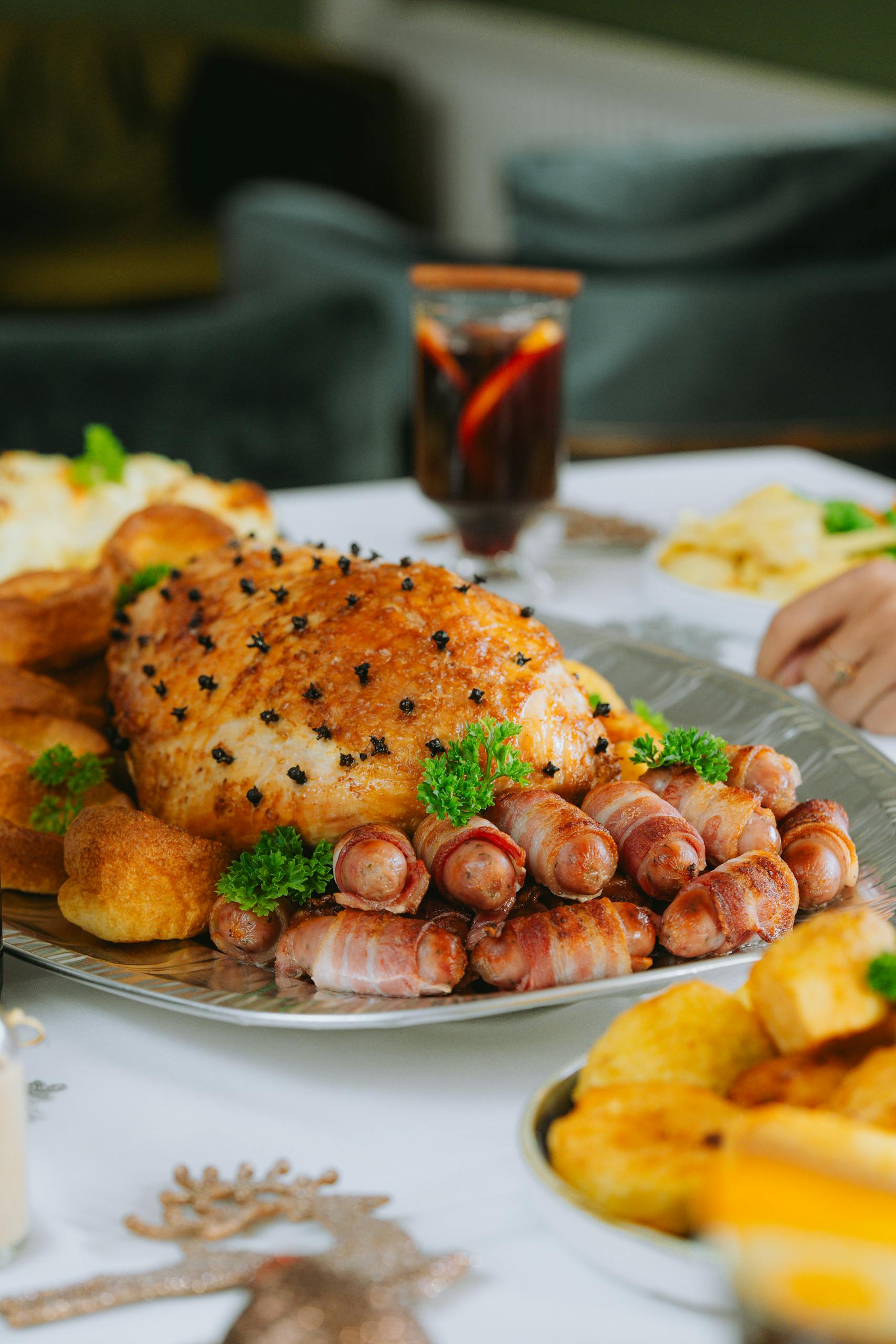 A perfectly cooked Christmas roast ham garnished with herbs and surrounded by assorted appetizers on a Staycation holiday table.