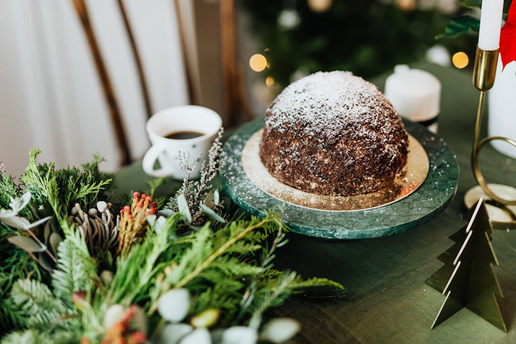 Festive Christmas pudding with coffee served on a green table, adorned with seasonal decorations.