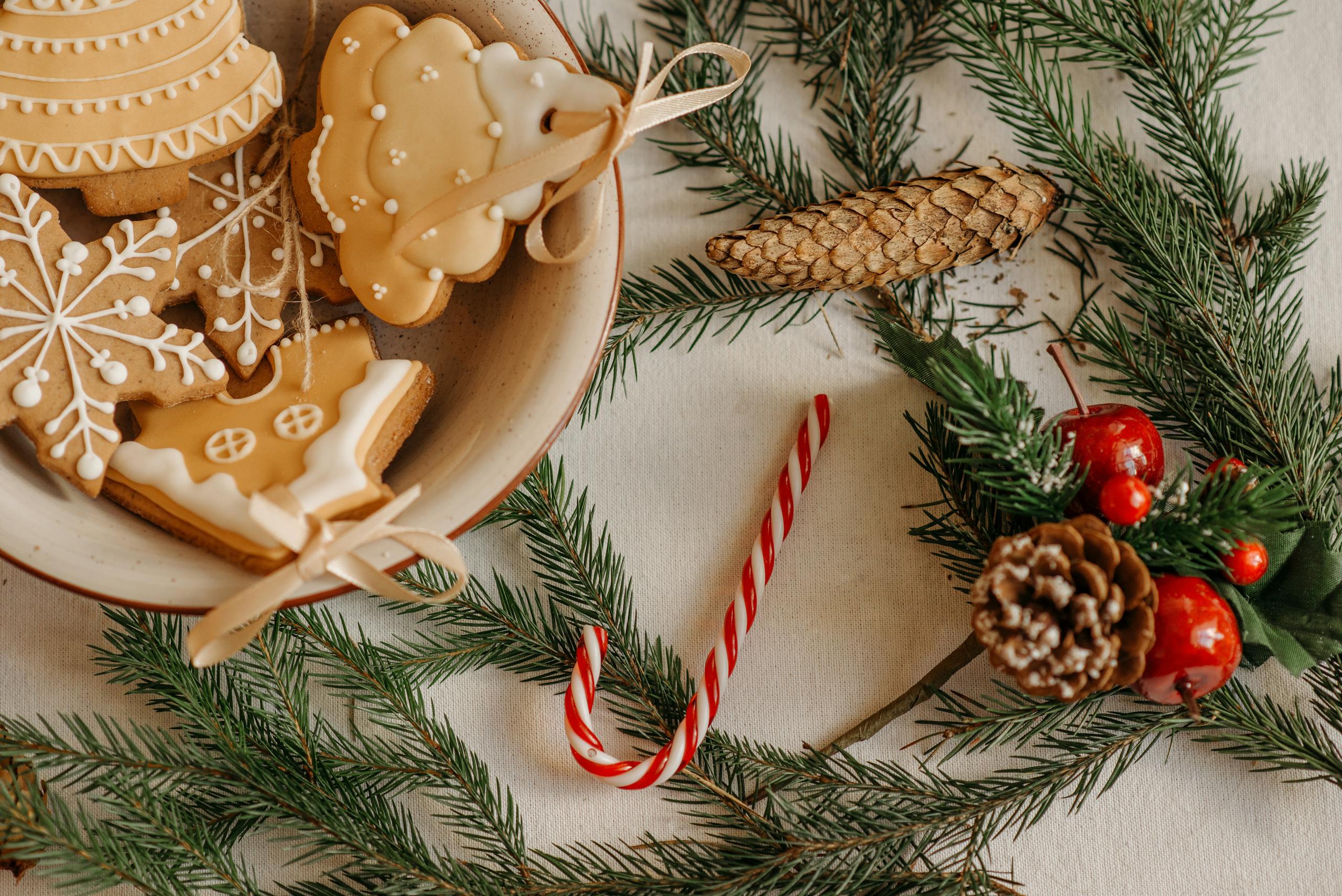 Christmas scene with cookies, pine branches, and candy cane on a table.