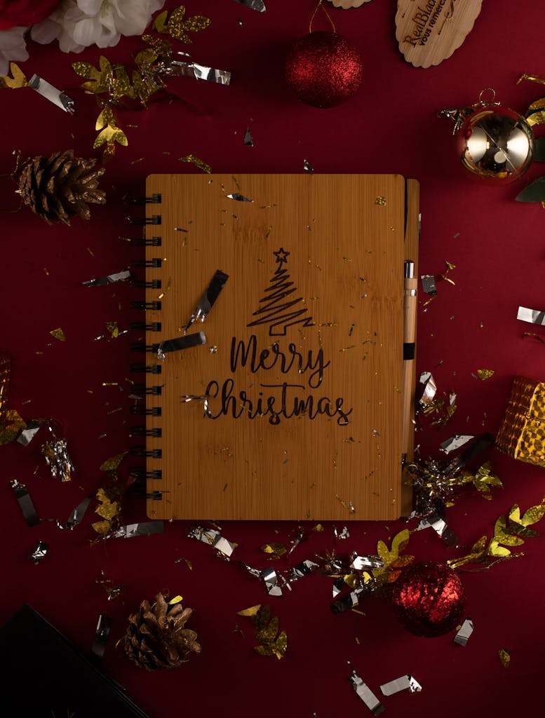 Merry Christmas notepad next to festive xmas decorations on a red background.