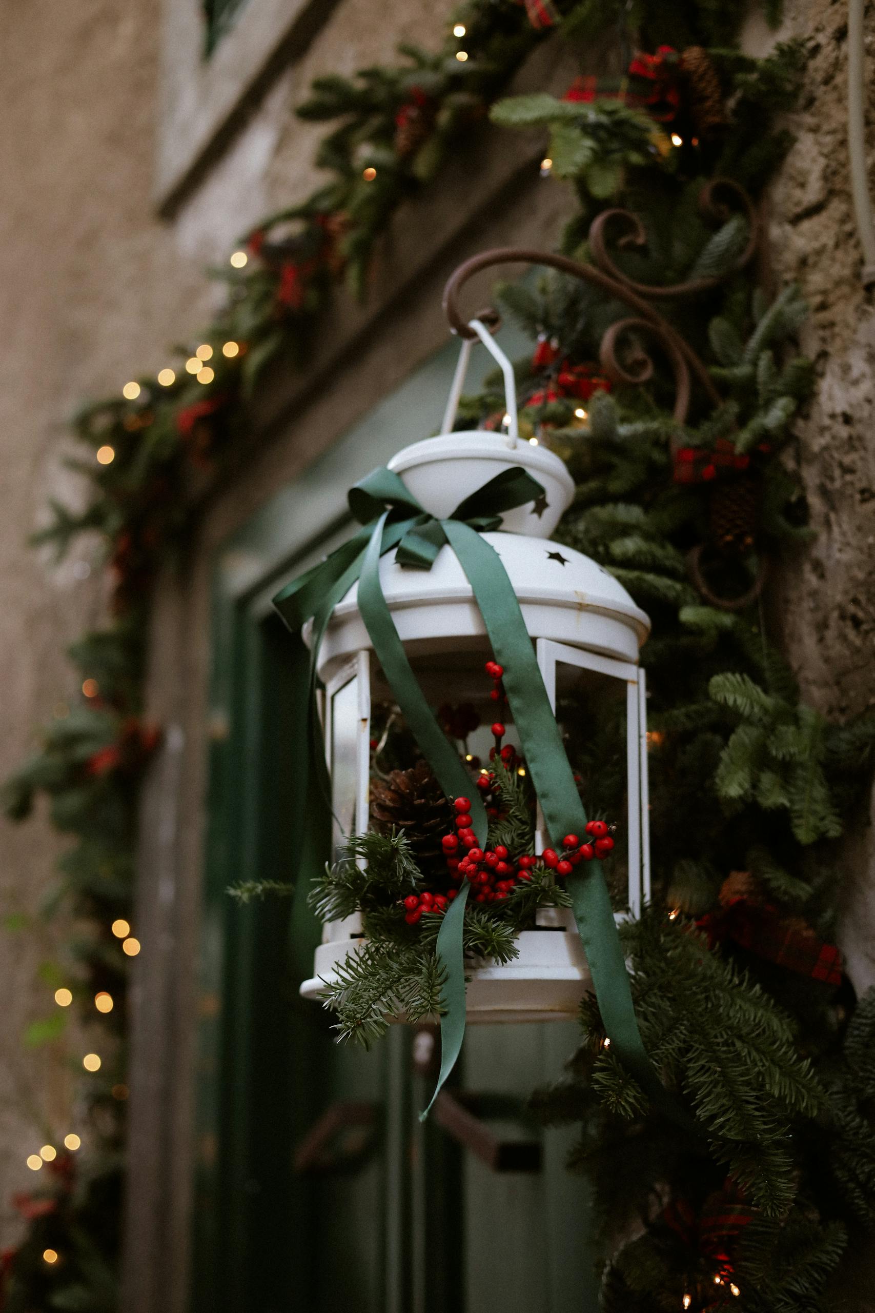 A white lantern adorned with pine branches and red berries in a holiday setting.