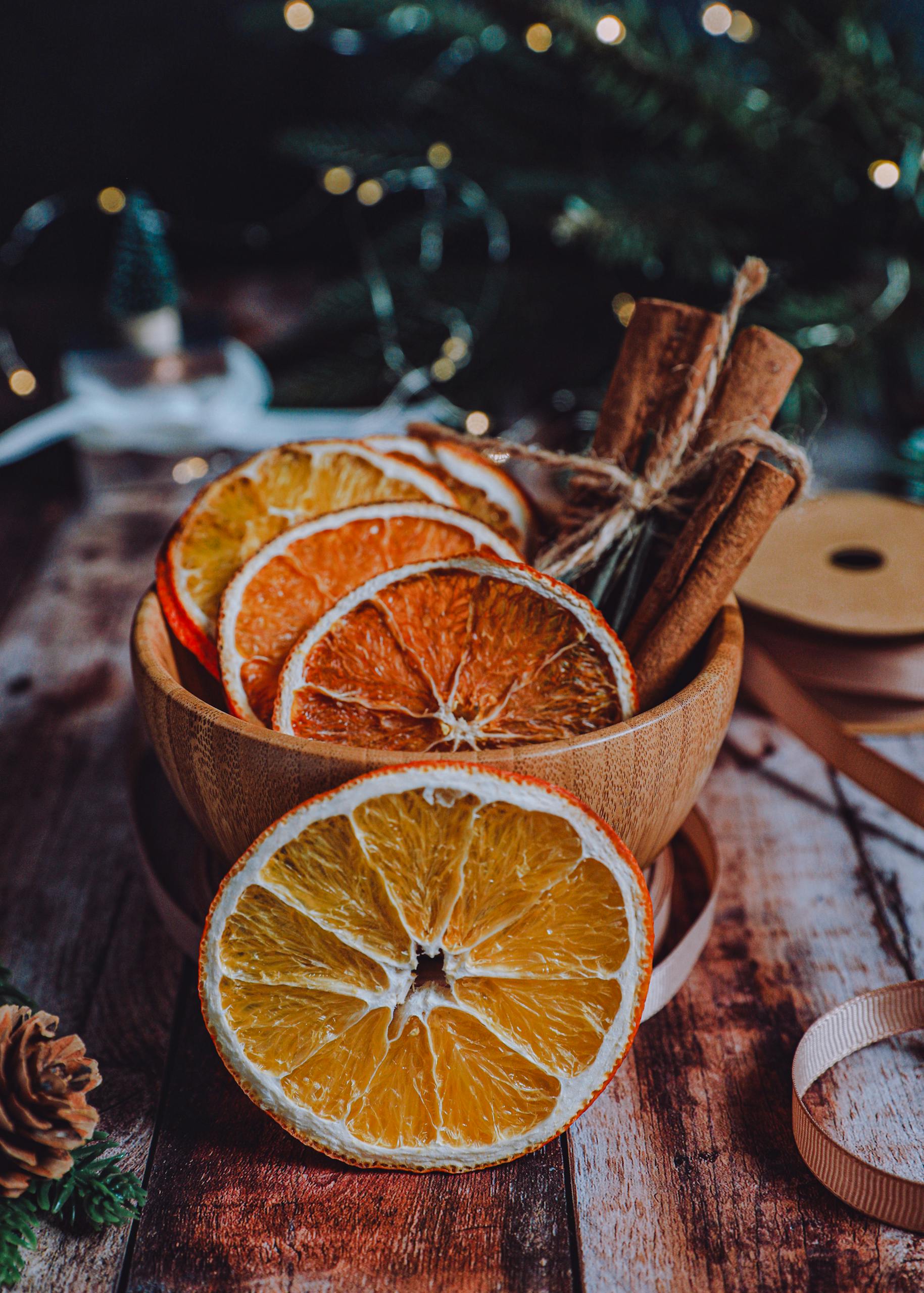 Wooden bowl with cinnamon sticks and dried orange slices for festive decoration.