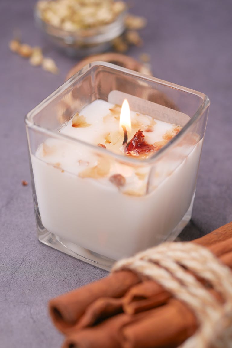 A close-up of a lit scented candle in a glass jar with cinnamon sticks, creating a cozy atmosphere.