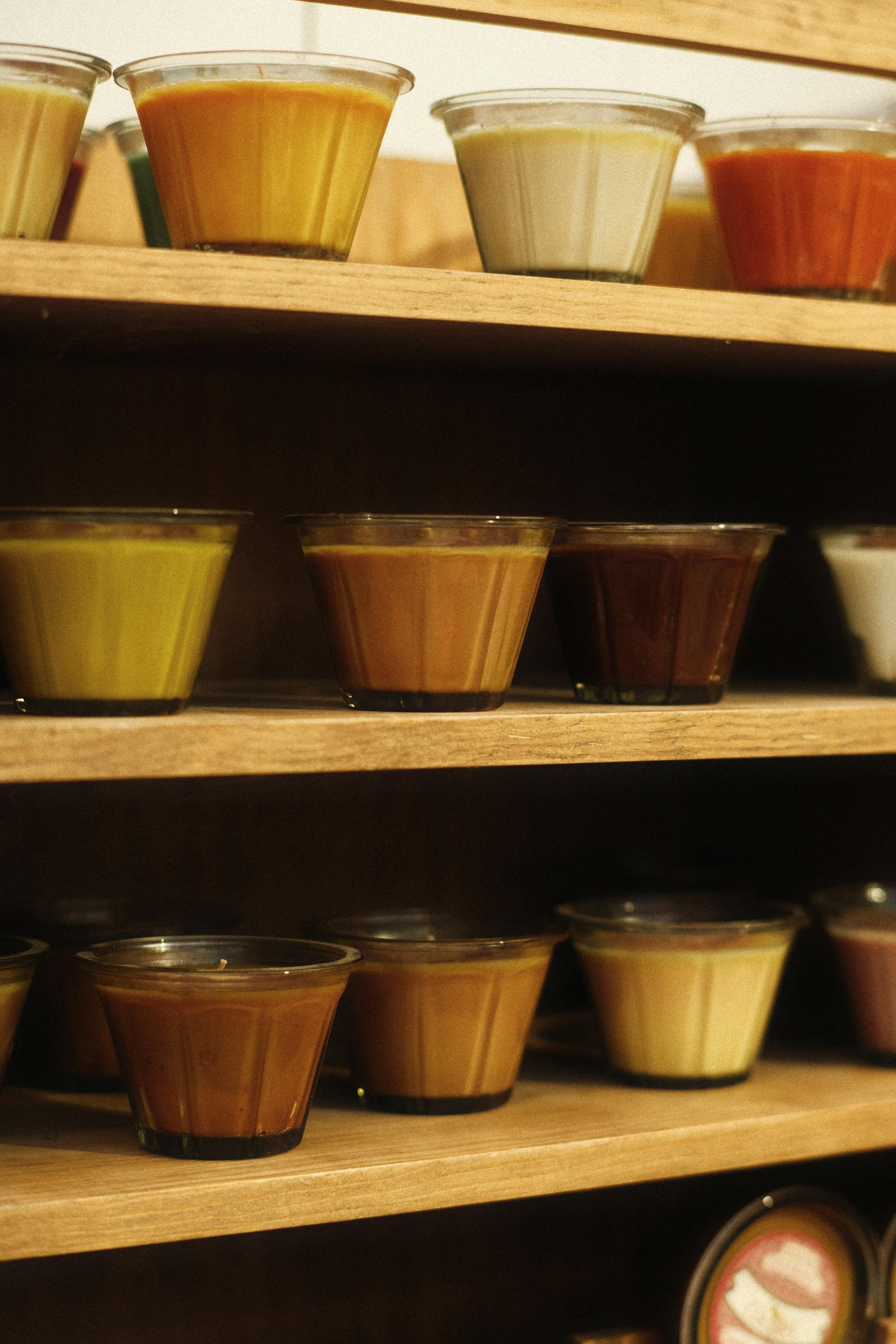 A vibrant array of candles in glass jars displayed on wooden shelves, creating a warm, inviting ambiance.