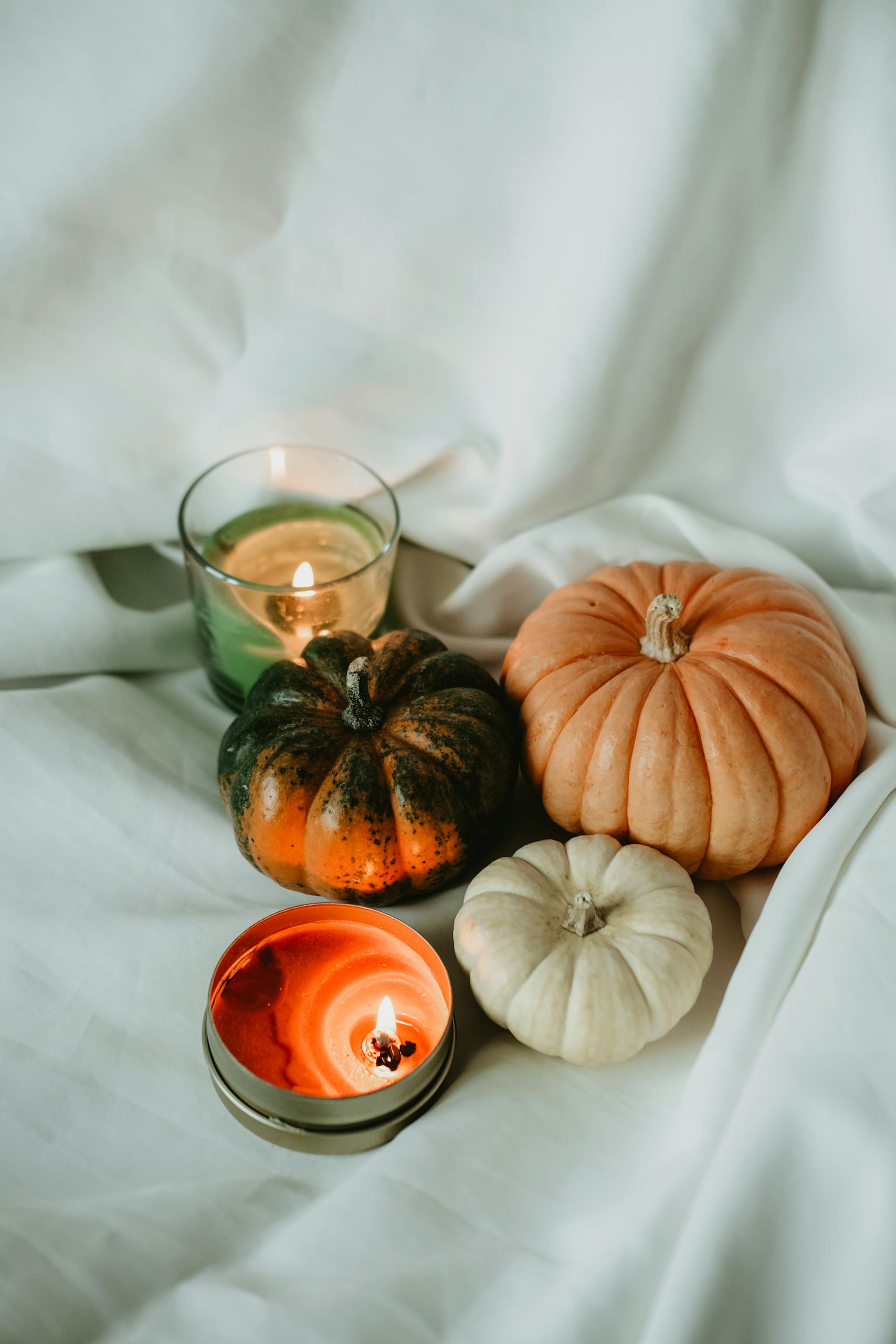A warm arrangement of pumpkins and candles set on a white cloth, perfect for autumn decoration.