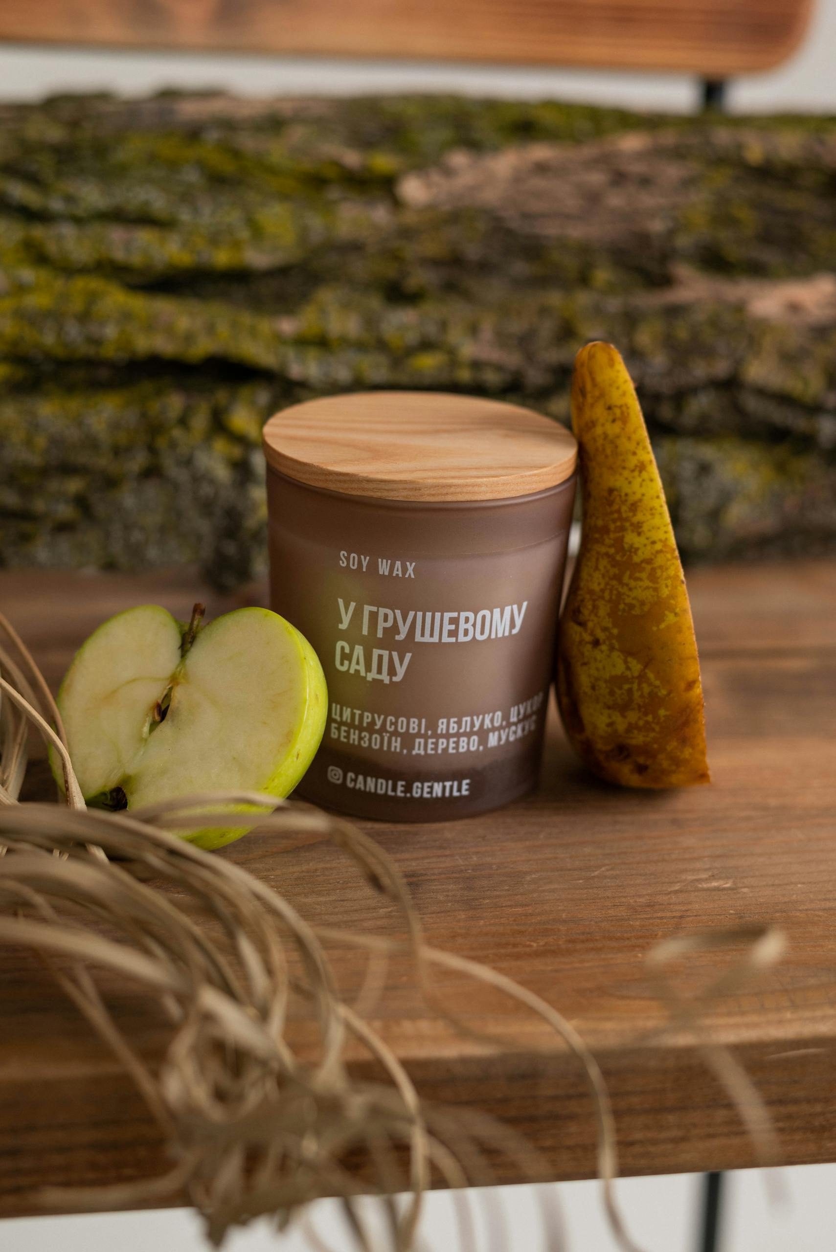 Soy wax candle with apple and pear on wooden surface, offering a rustic feel.