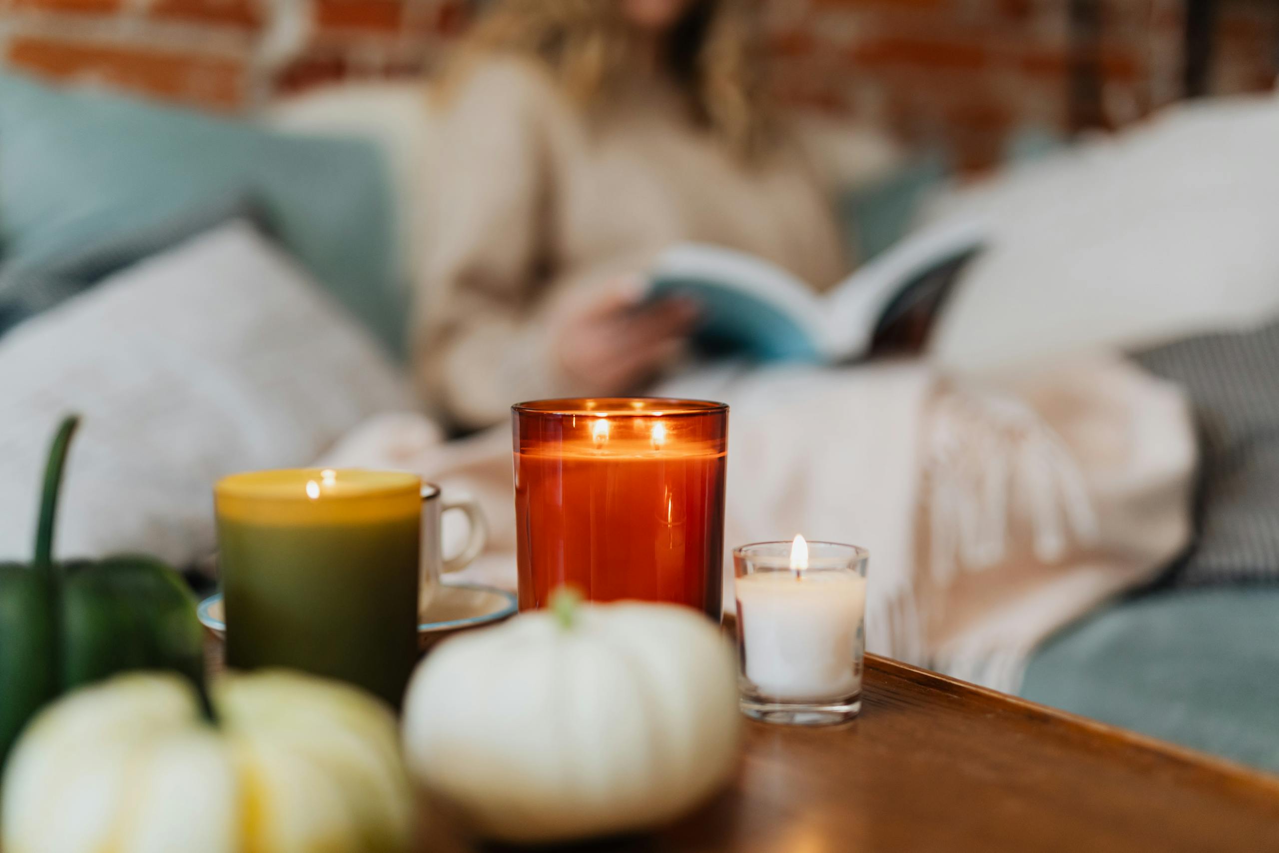 Warm autumn scene with candles, pumpkins, and a person reading in a cozy setting.