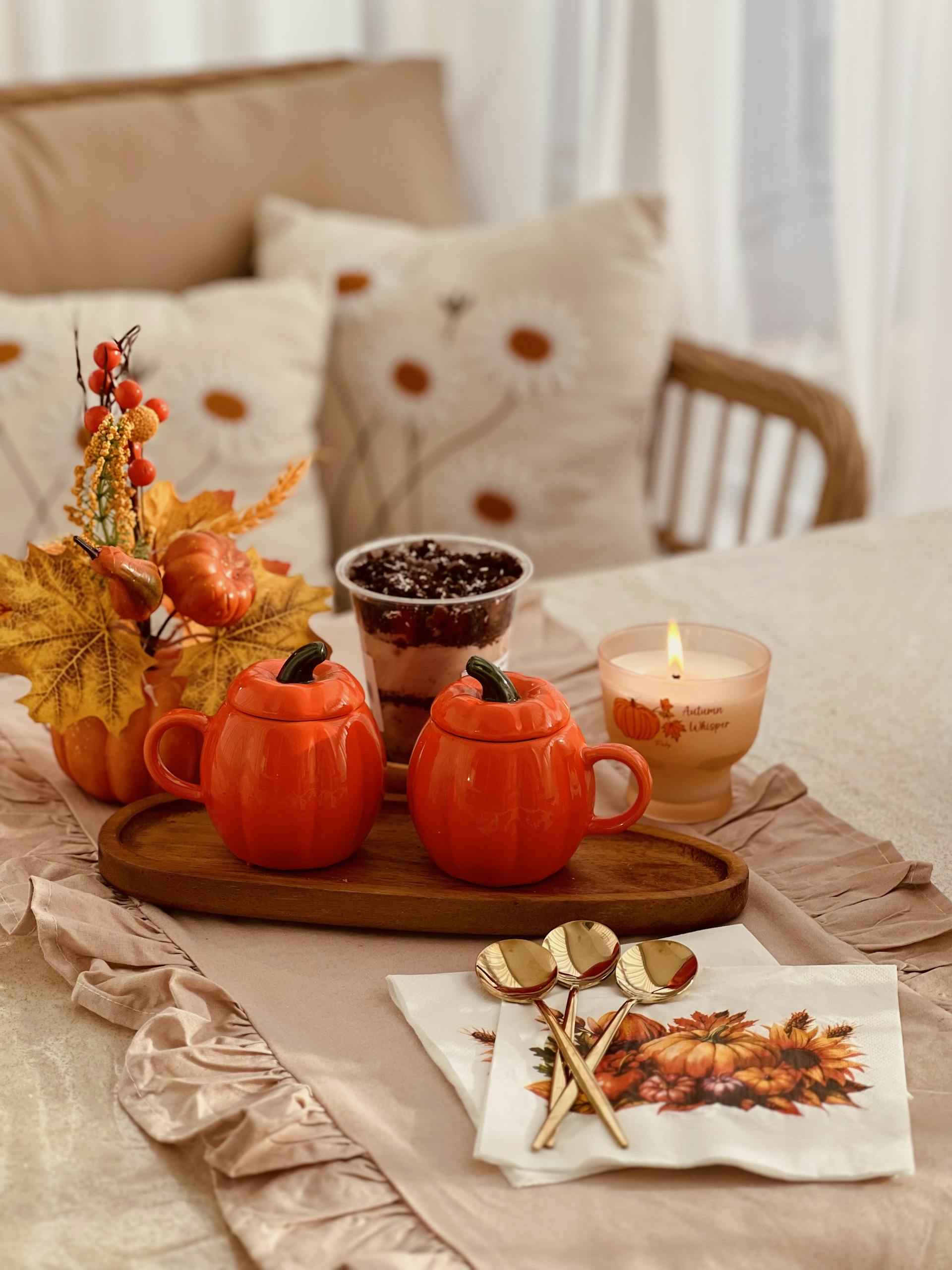 Warm autumn setting with pumpkin mugs, candle, and fall leaves on a cozy table.