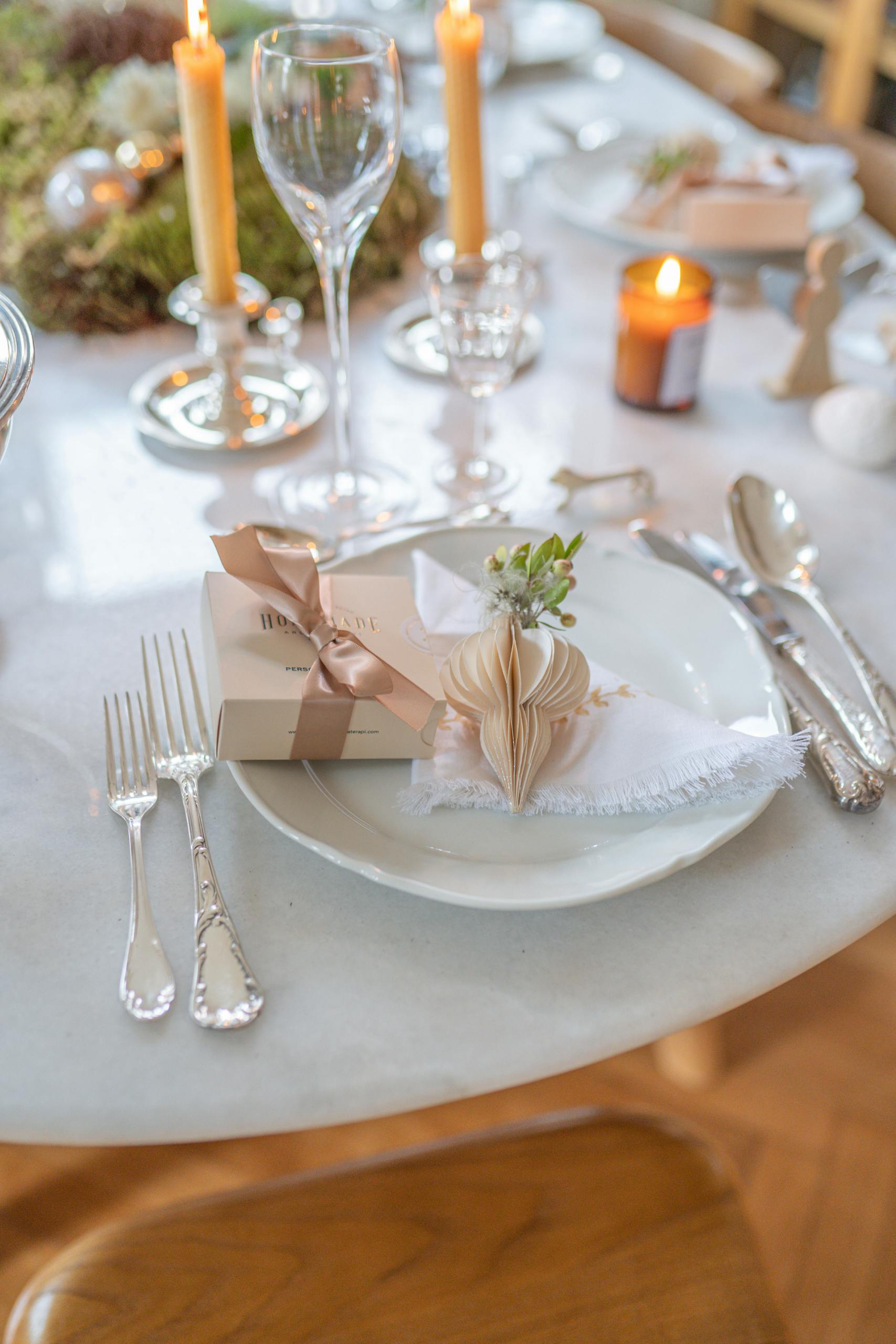 A beautifully decorated table for a special occasion with candles, gift, and elegant cutlery.