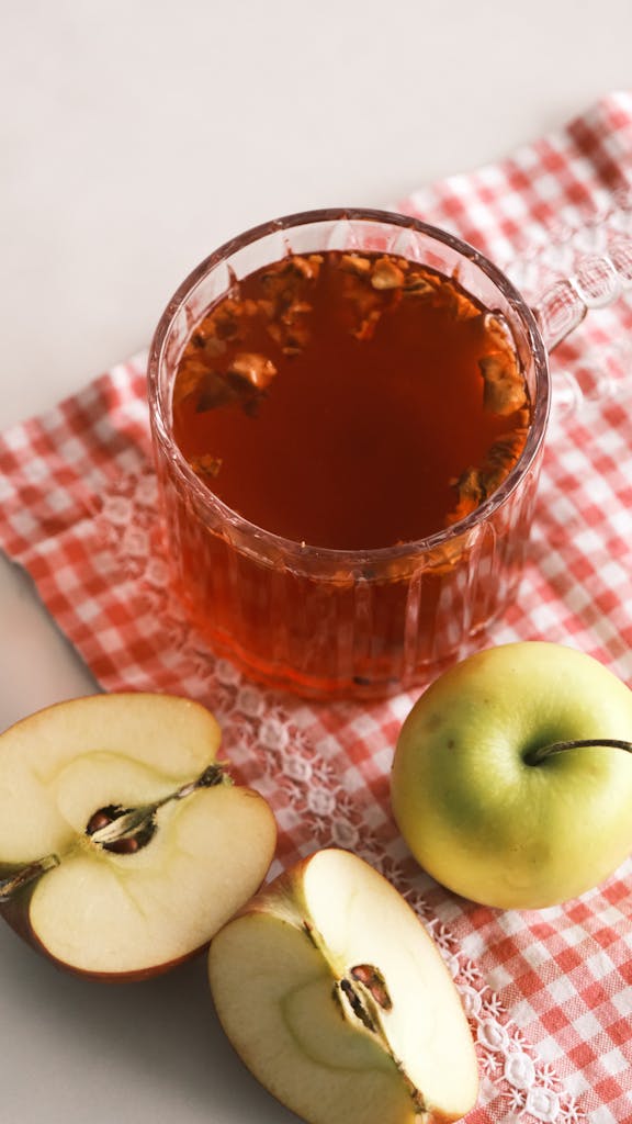 A cup of apple tea with fresh green apples on red checkered cloth.