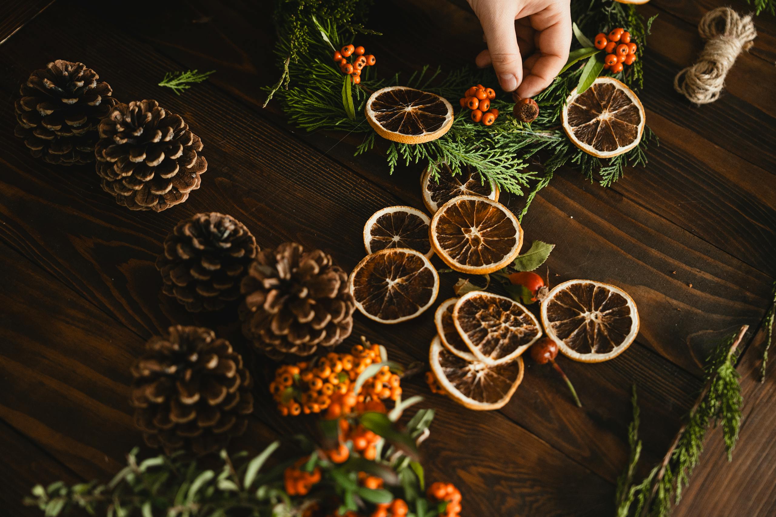 A handmade wreath with pinecones and dried oranges on a rustic wooden table.