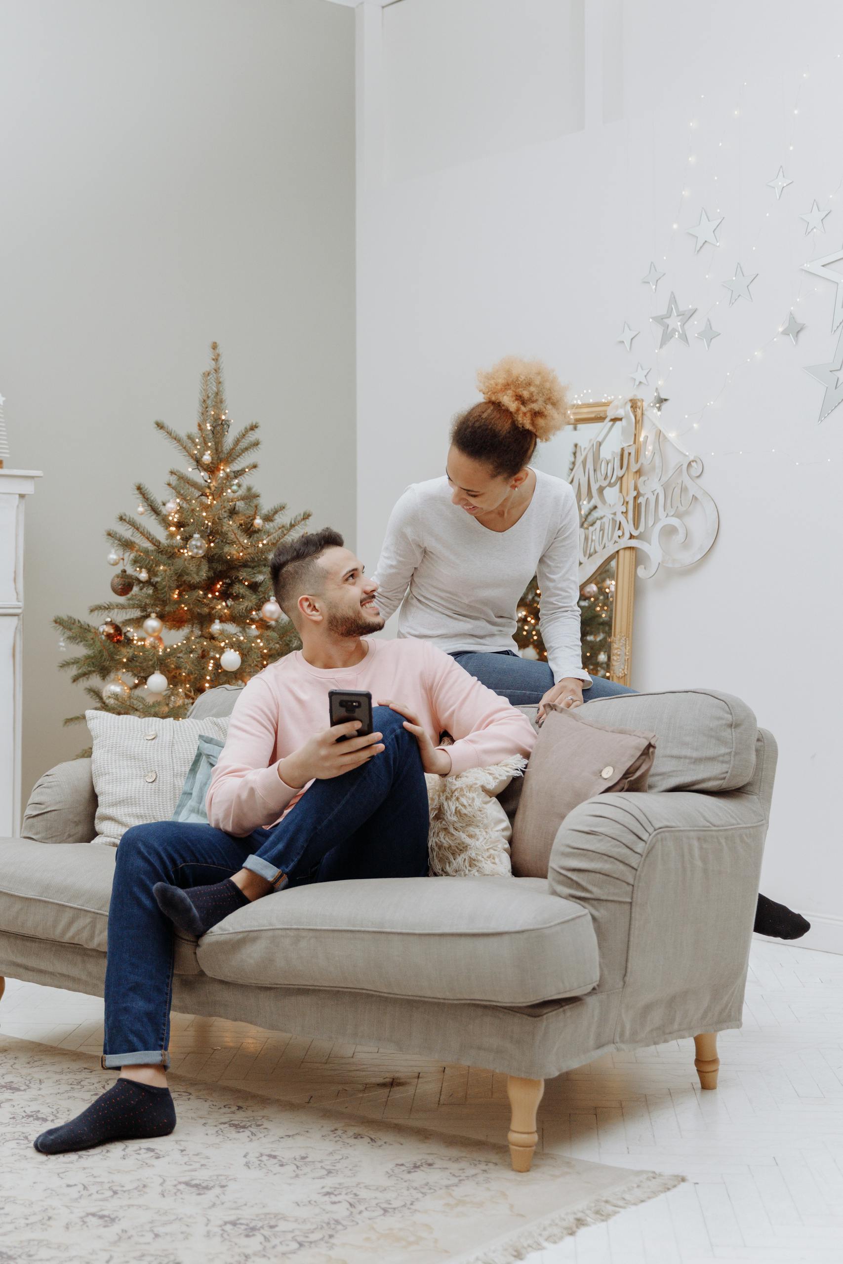 A happy couple sitting on a sofa, enjoying a cozy Christmas setting at home.