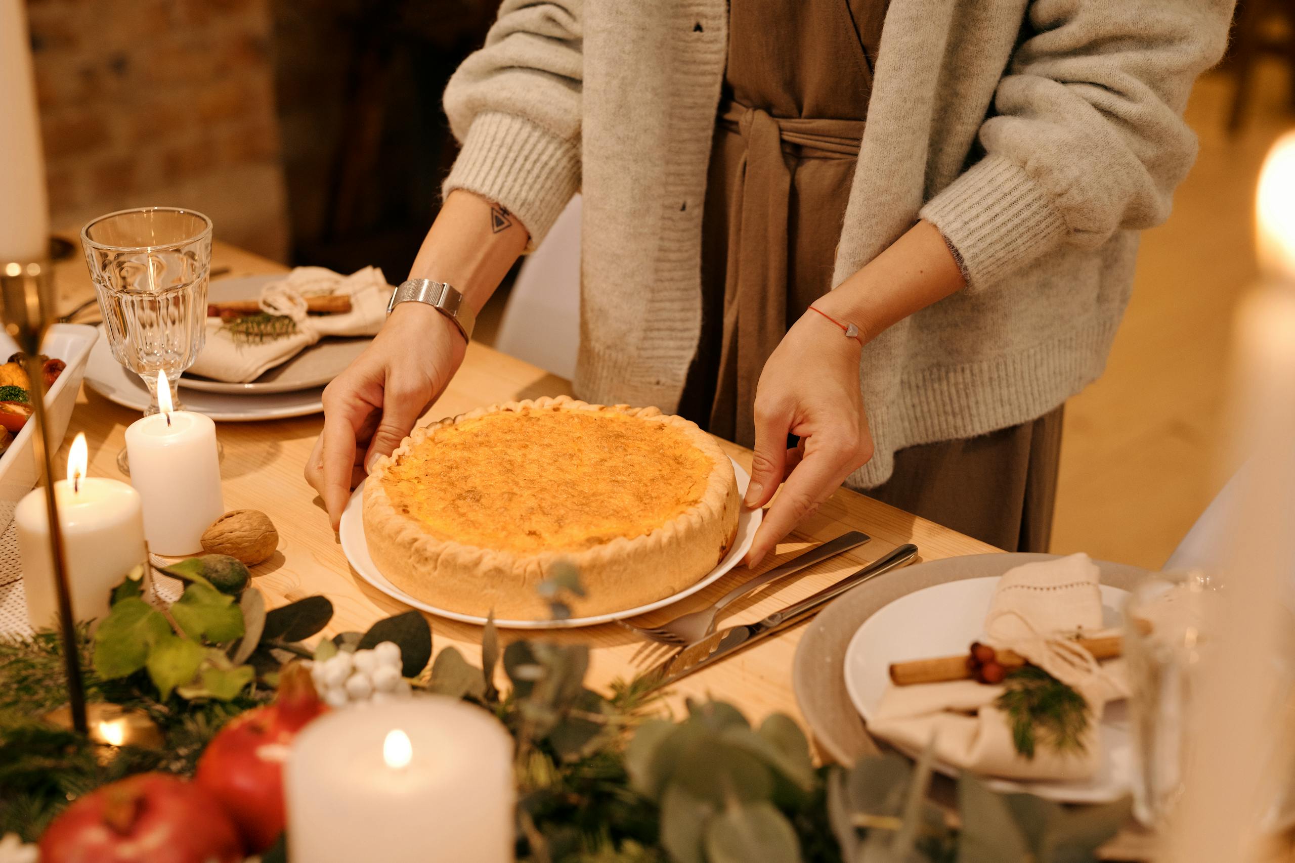 A person setting a Turkey pie on a beautifully decorated holiday dinner table with candles and winter greenery.
