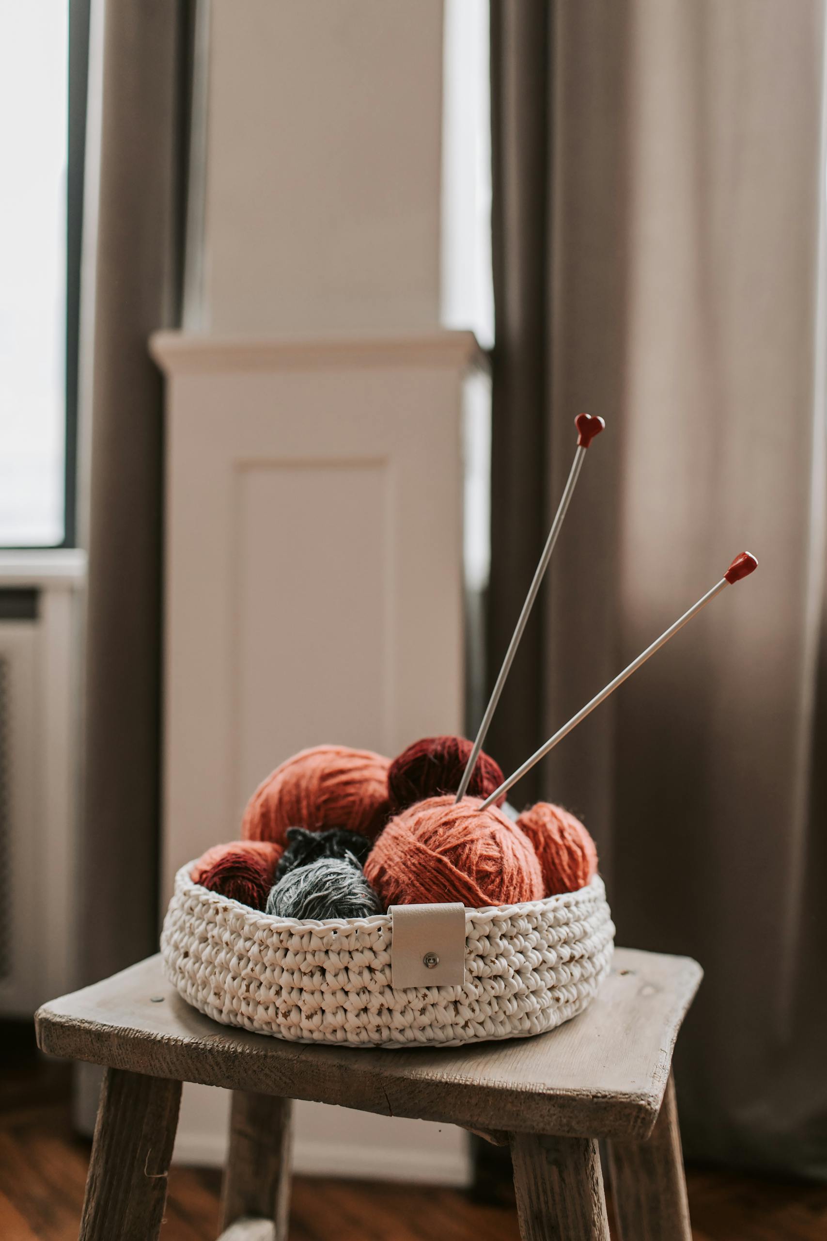 Close-up of a knitted basket on a wooden chair with colorful yarn and knitting needles.