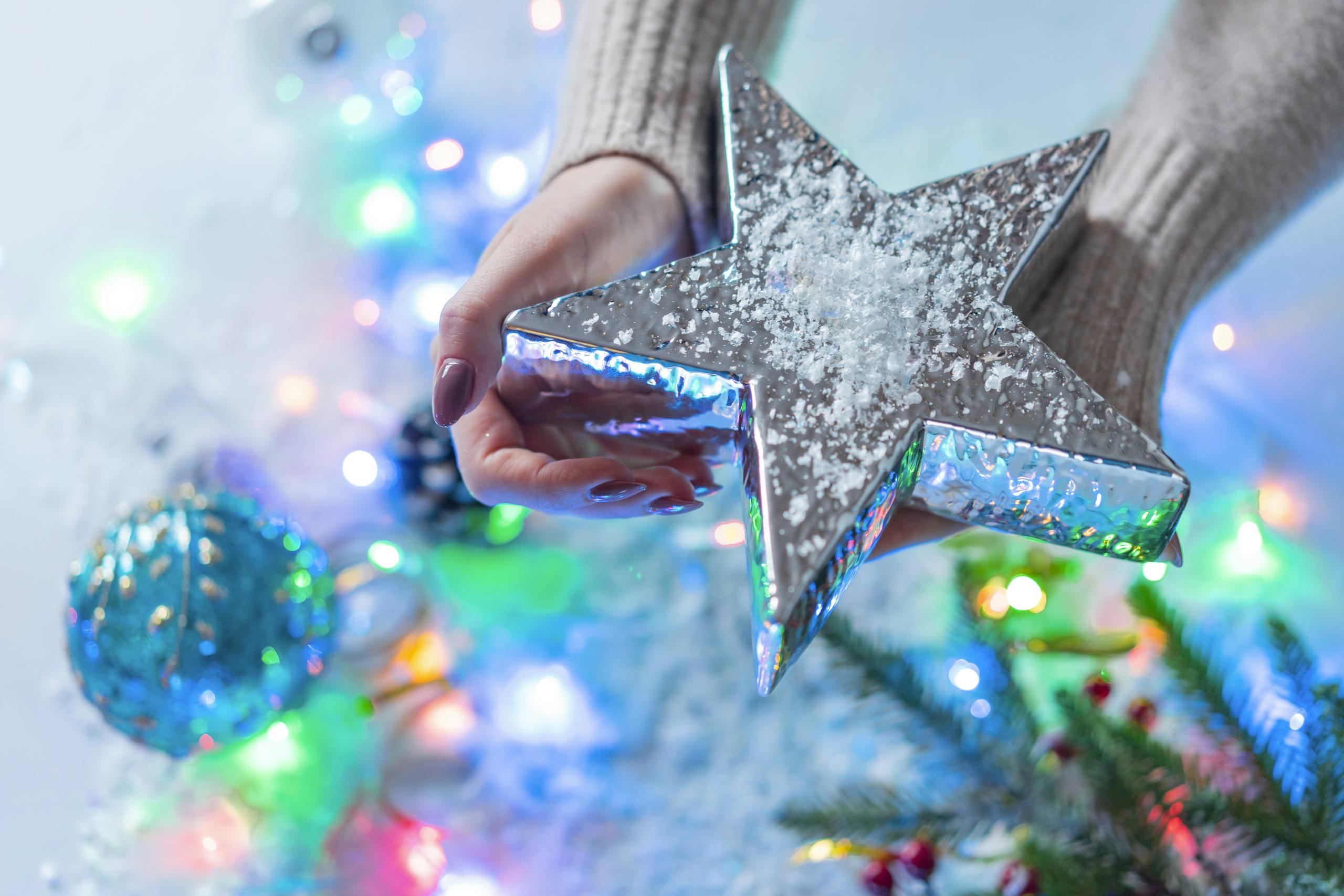 Close-up of hand holding a sparkling Christmas star with colorful holiday lights.