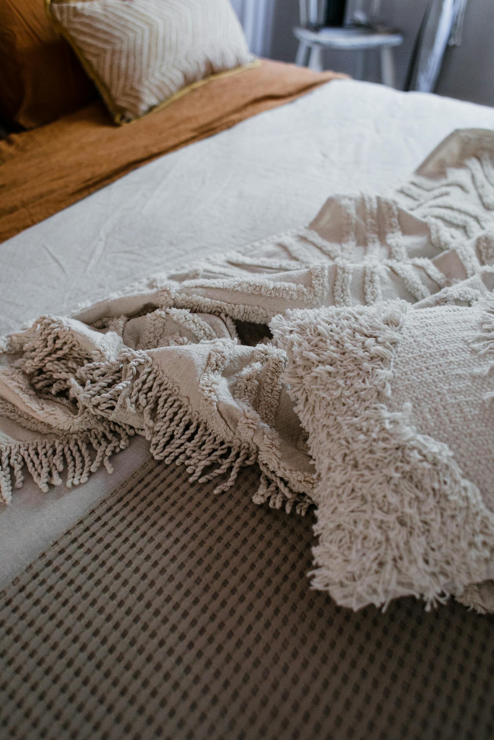 Close-up of textured knit and linen blankets on an indoor bed setting.