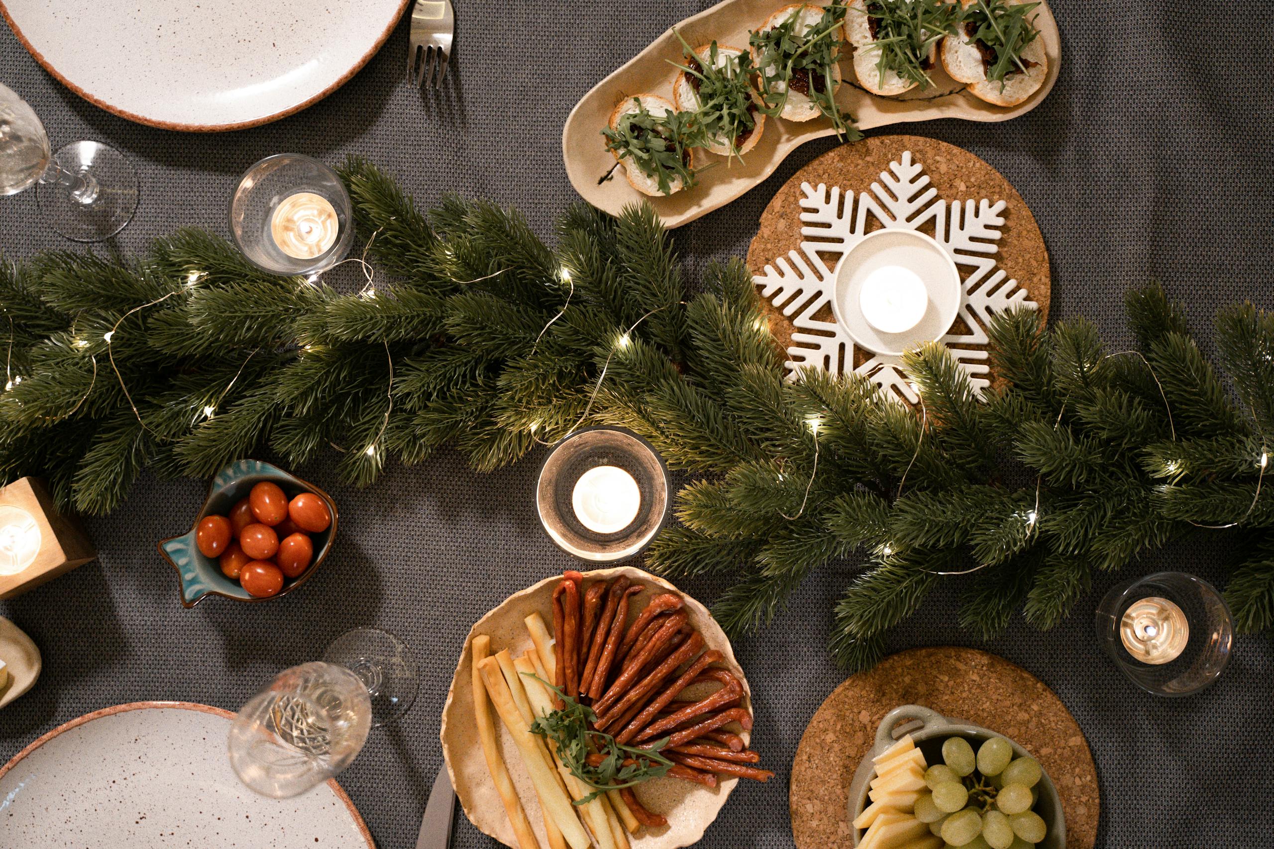 Elegant holiday table setting with festive greenery, candles, and snacks.