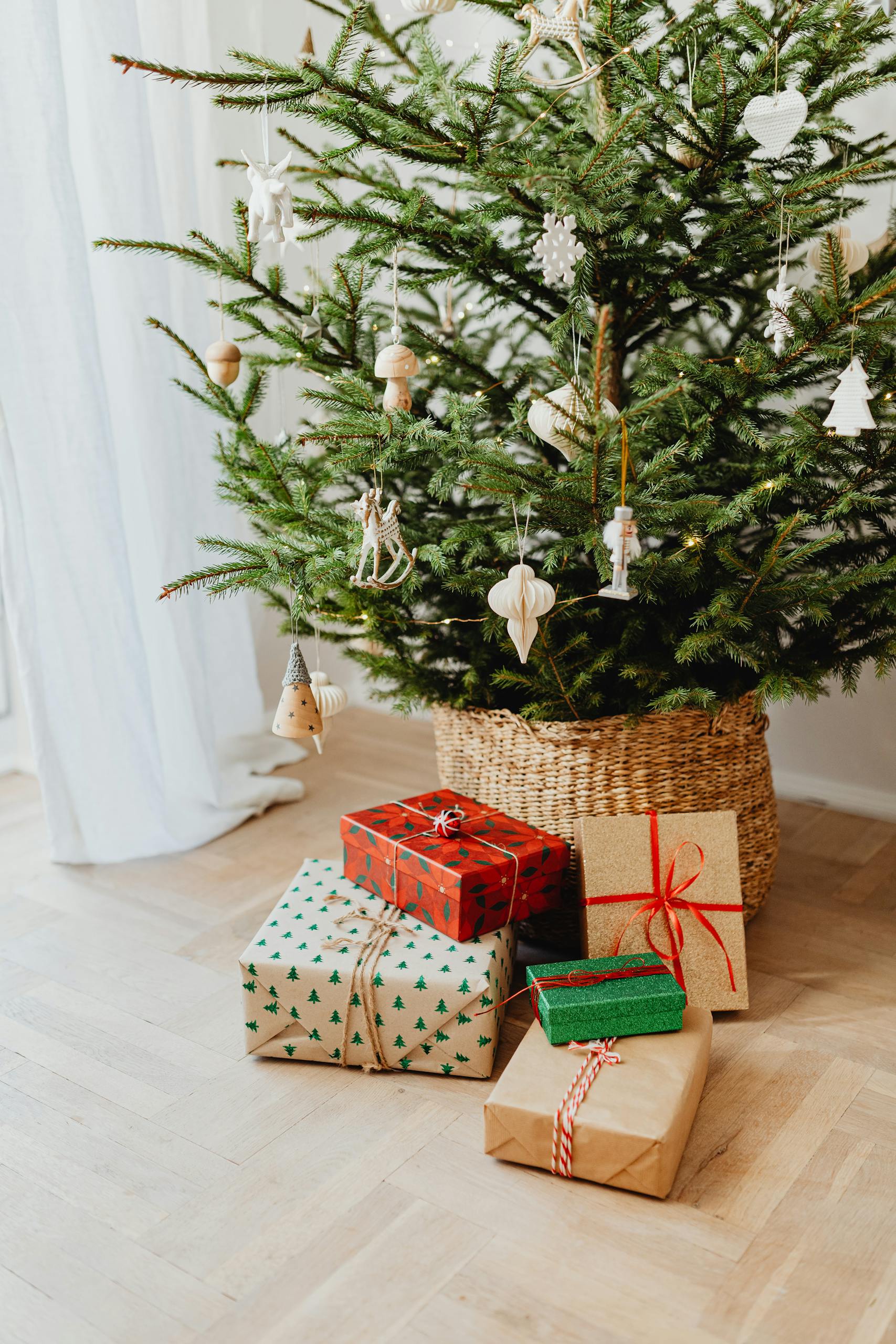 Festive Christmas tree adorned with ornaments and wrapped gift boxes under a basket base.
