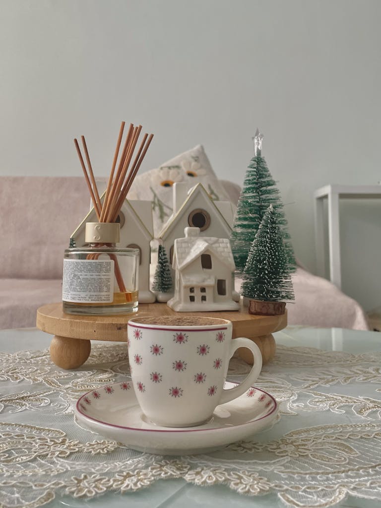 Festive setup with ceramic cup, mini trees, and reed diffuser on table.