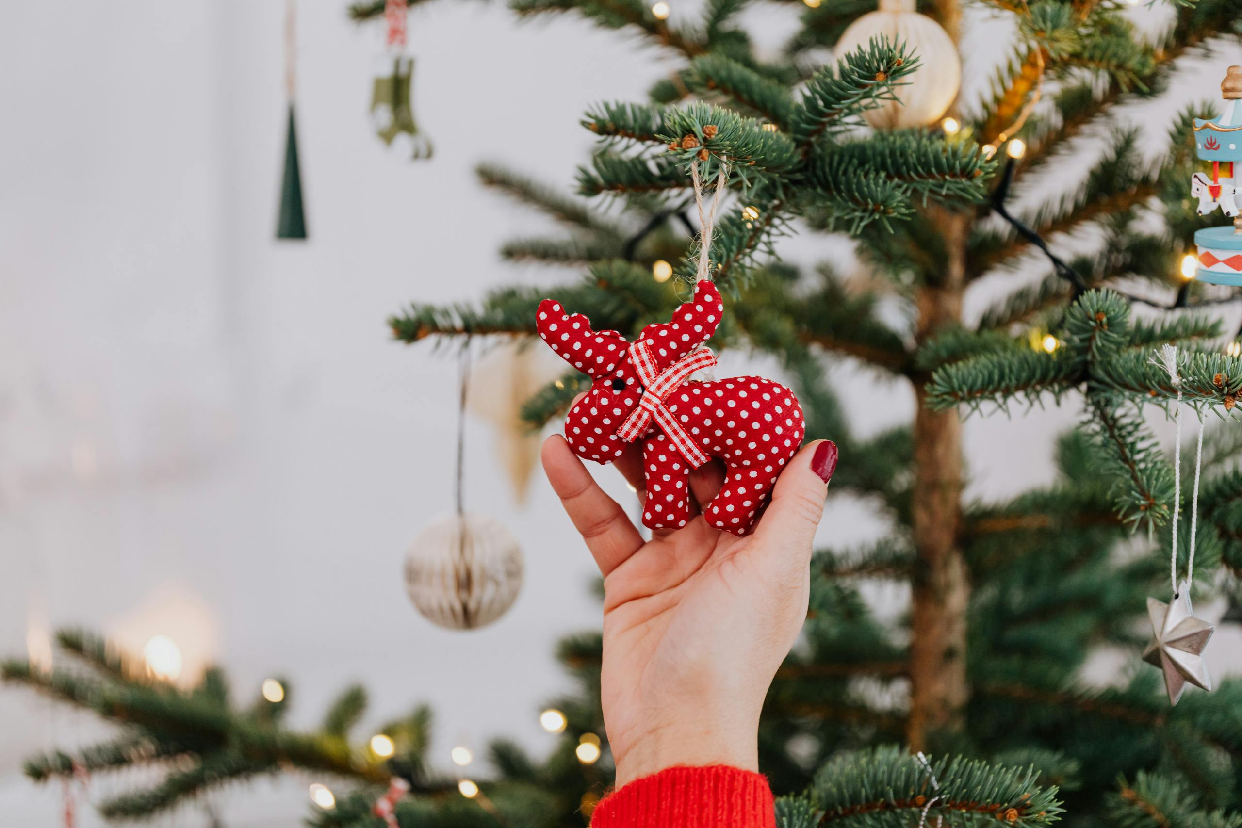 Hand decorating Christmas tree with red polka dot ornament, creating a festive holiday atmosphere.