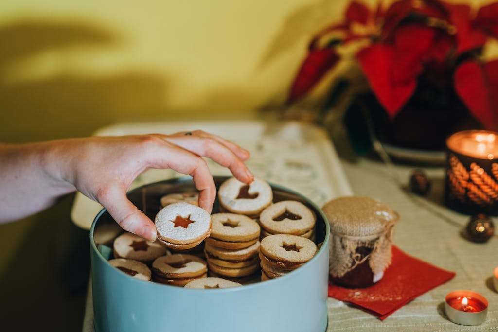 Hand picking delicious star-shaped Christmas cookies from a festive tin, perfect for holiday celebrations.