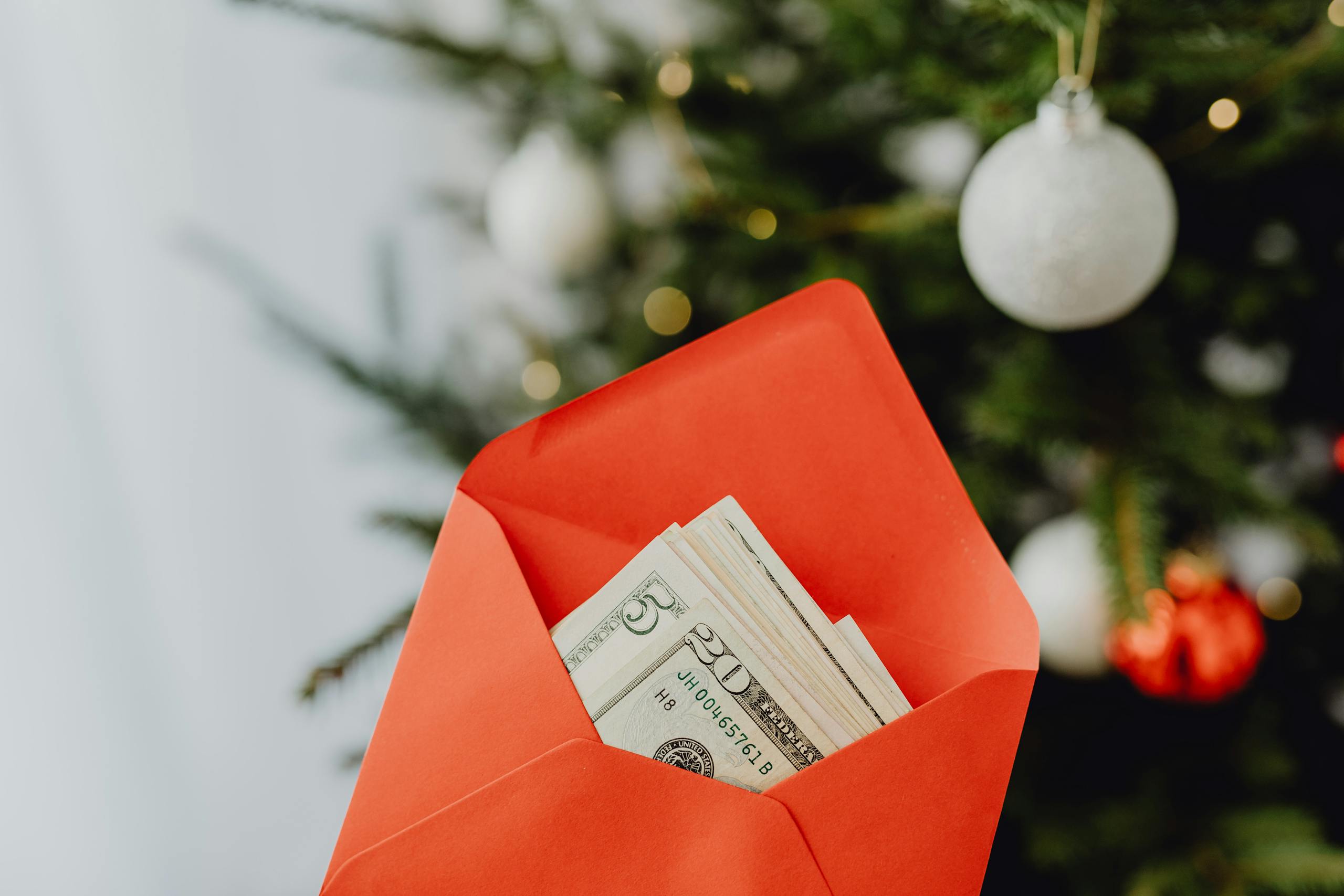 Red envelope with cash set against a decorated Christmas tree symbolizes festive gifting.