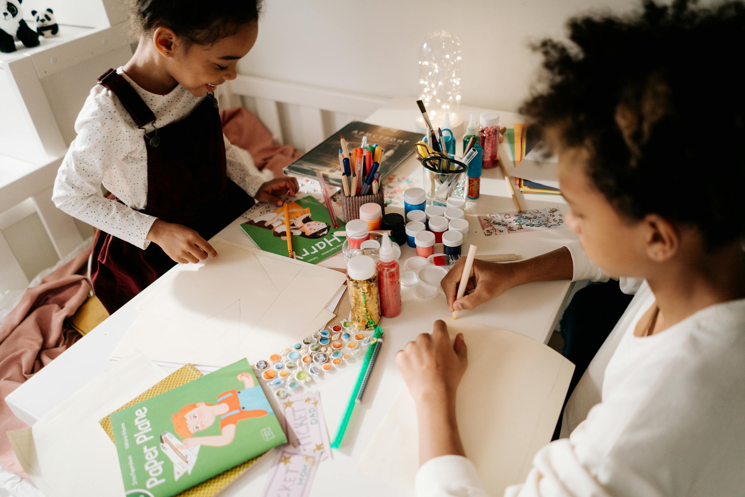 Two children enjoying arts and crafts with vibrant materials on a table indoors.