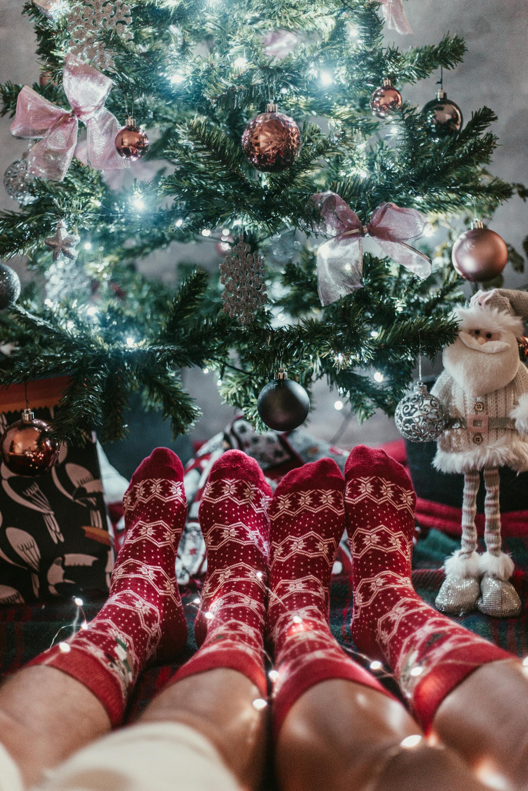 Two people in holiday socks relaxing by a Christmas tree.