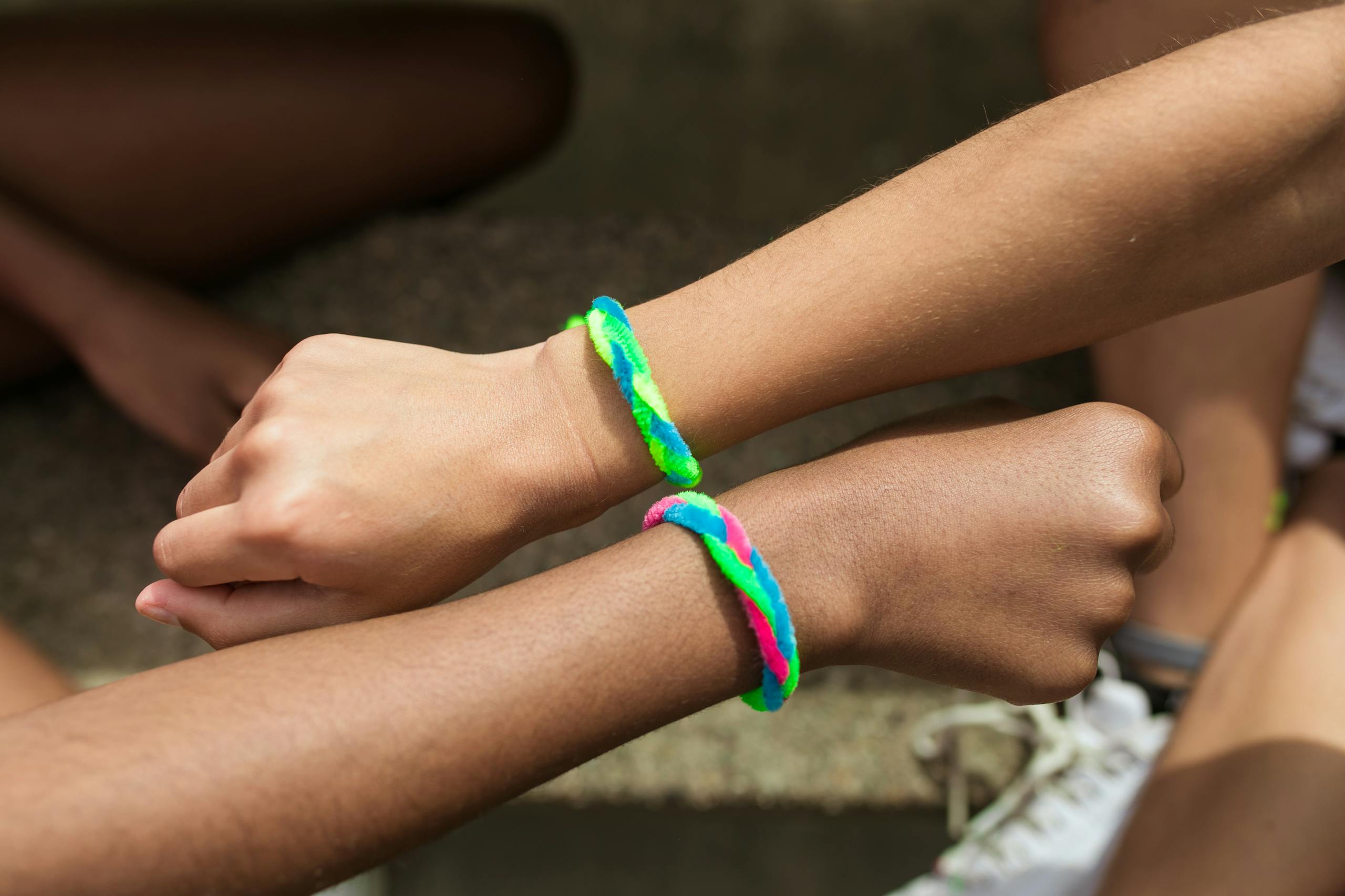 Two wrists with colorful friendship bracelets in a close-up view, symbolizing friendship.