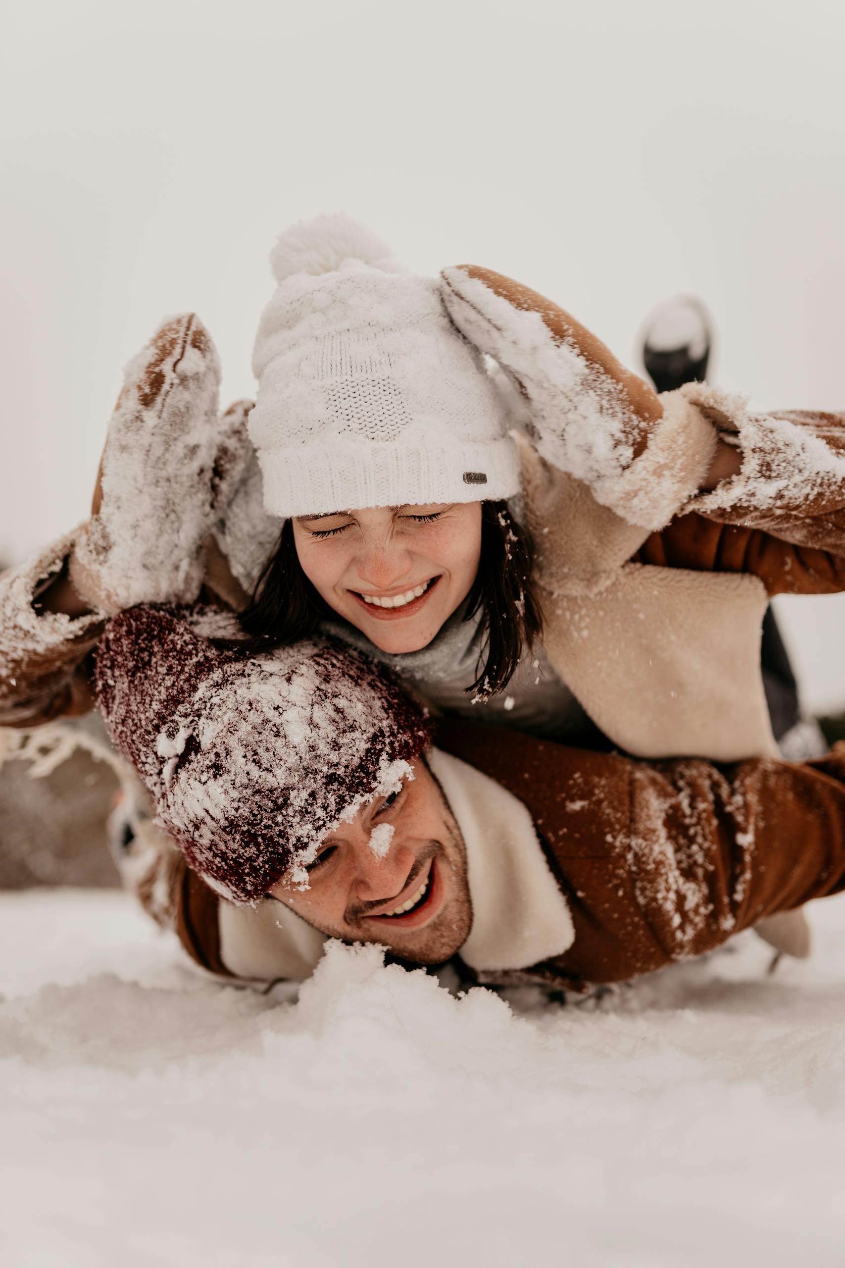 Young couple playfully enjoying a snowy winter day, dressed warmly in hats and gloves.