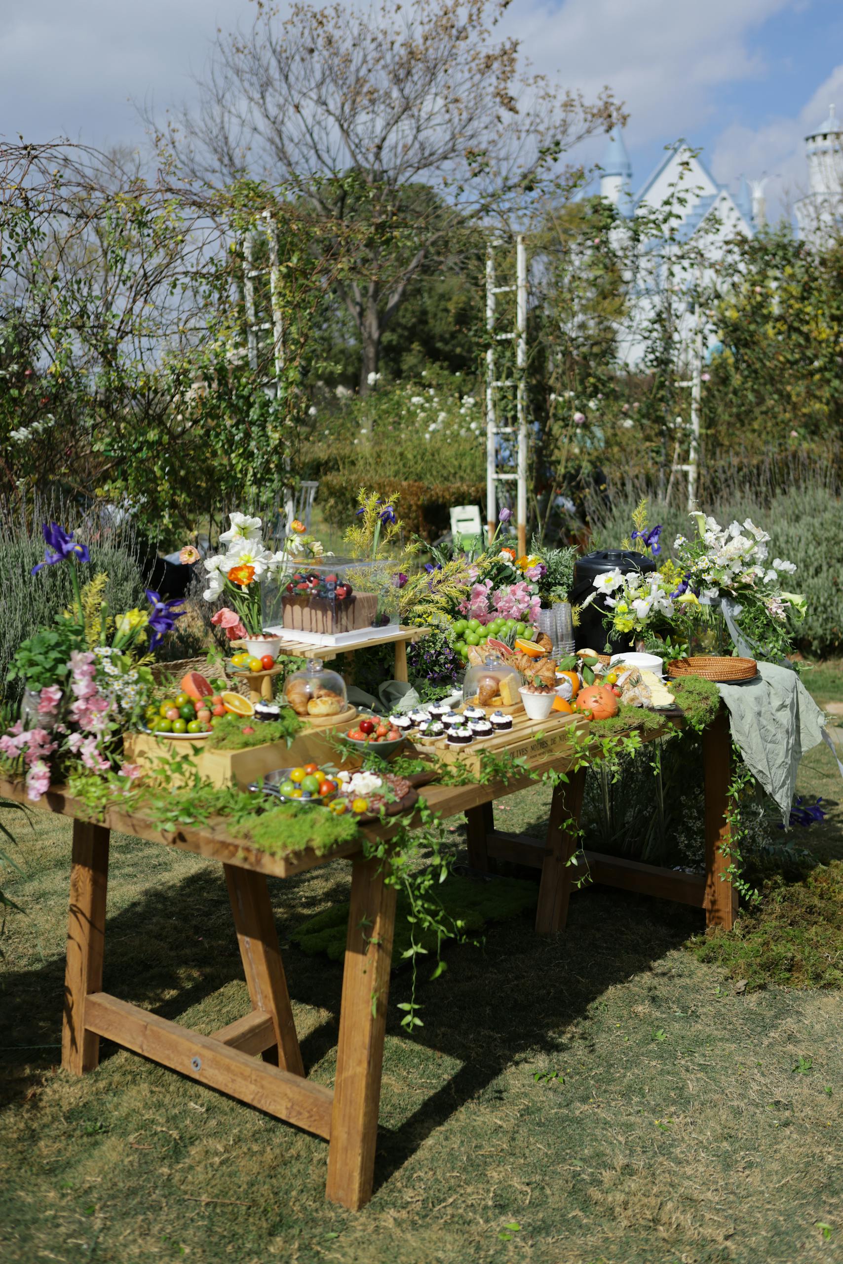 A charming garden table set with flowers and assorted food, perfect for outdoor events.