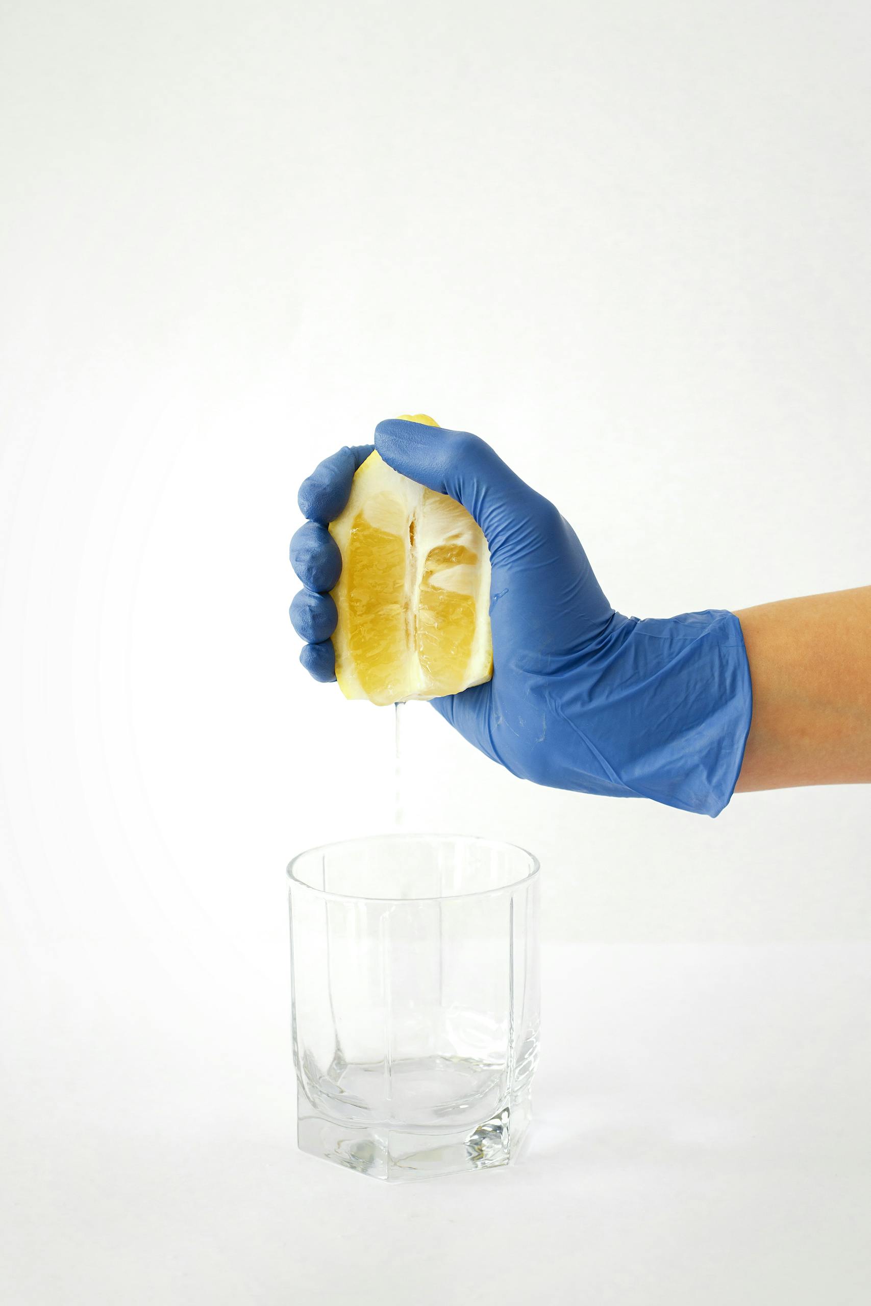 A hand in blue gloves squeezing a lemon wedge into a glass, emphasizing cleanliness and freshness.