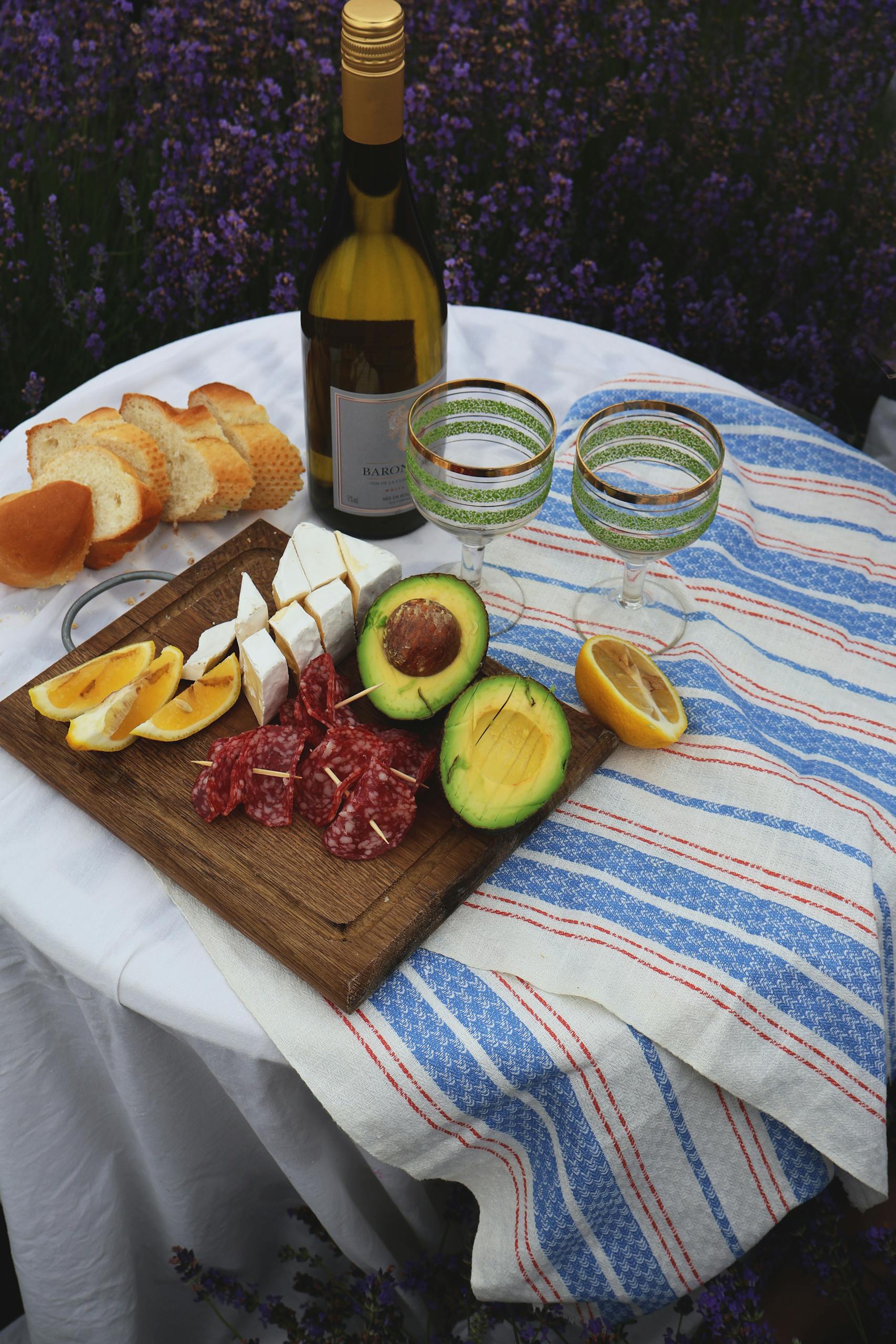 A rustic outdoor picnic setup with wine, cheese, and fresh produce on a table.
