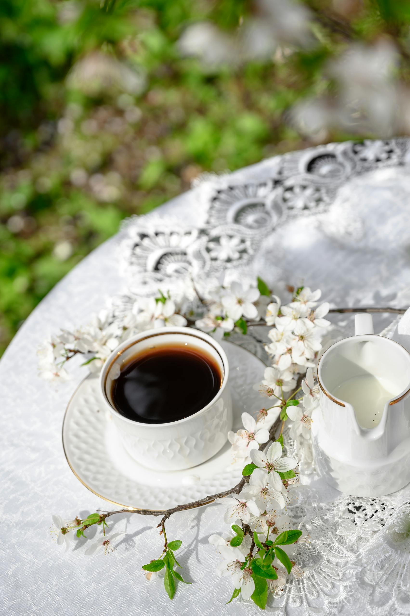 A serene coffee setup with fresh blossoms and lace tablecloth, capturing a peaceful morning vibe.