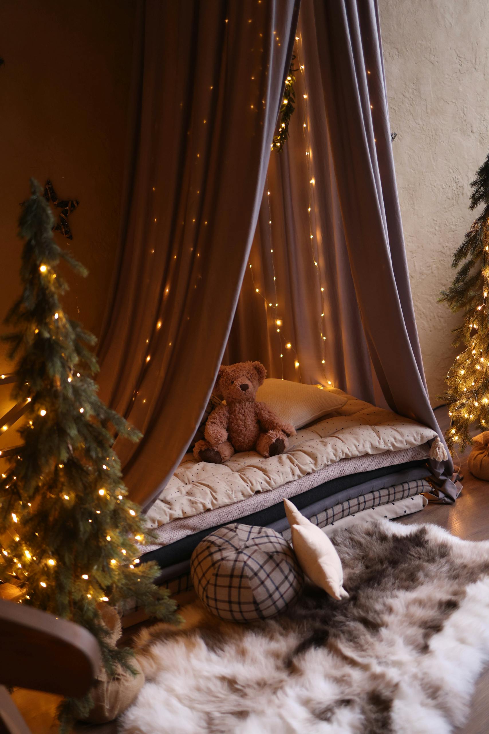 A warm and inviting indoor tent setup with a teddy bear, fairy lights, and plush decor for a serene ambiance.