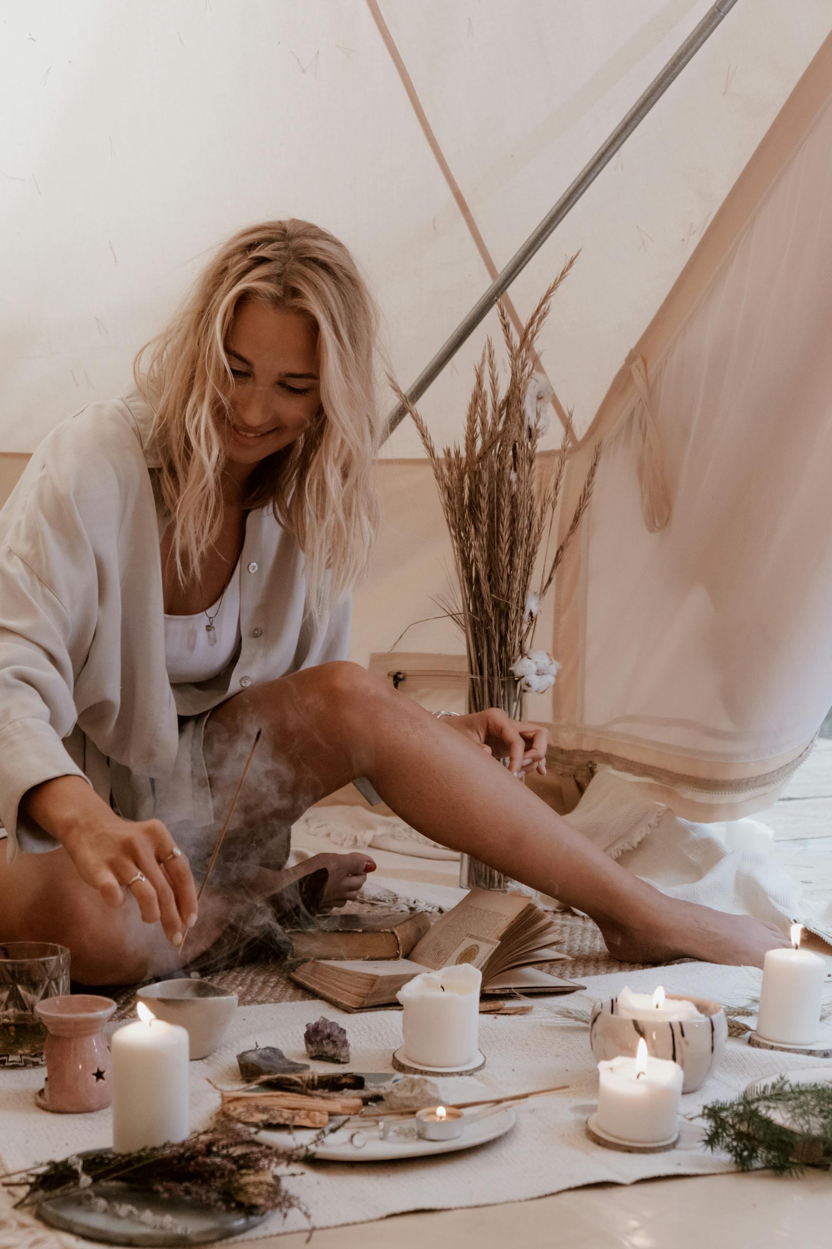 A woman enjoys a cozy indoor setting with candles and natural decor for relaxation.