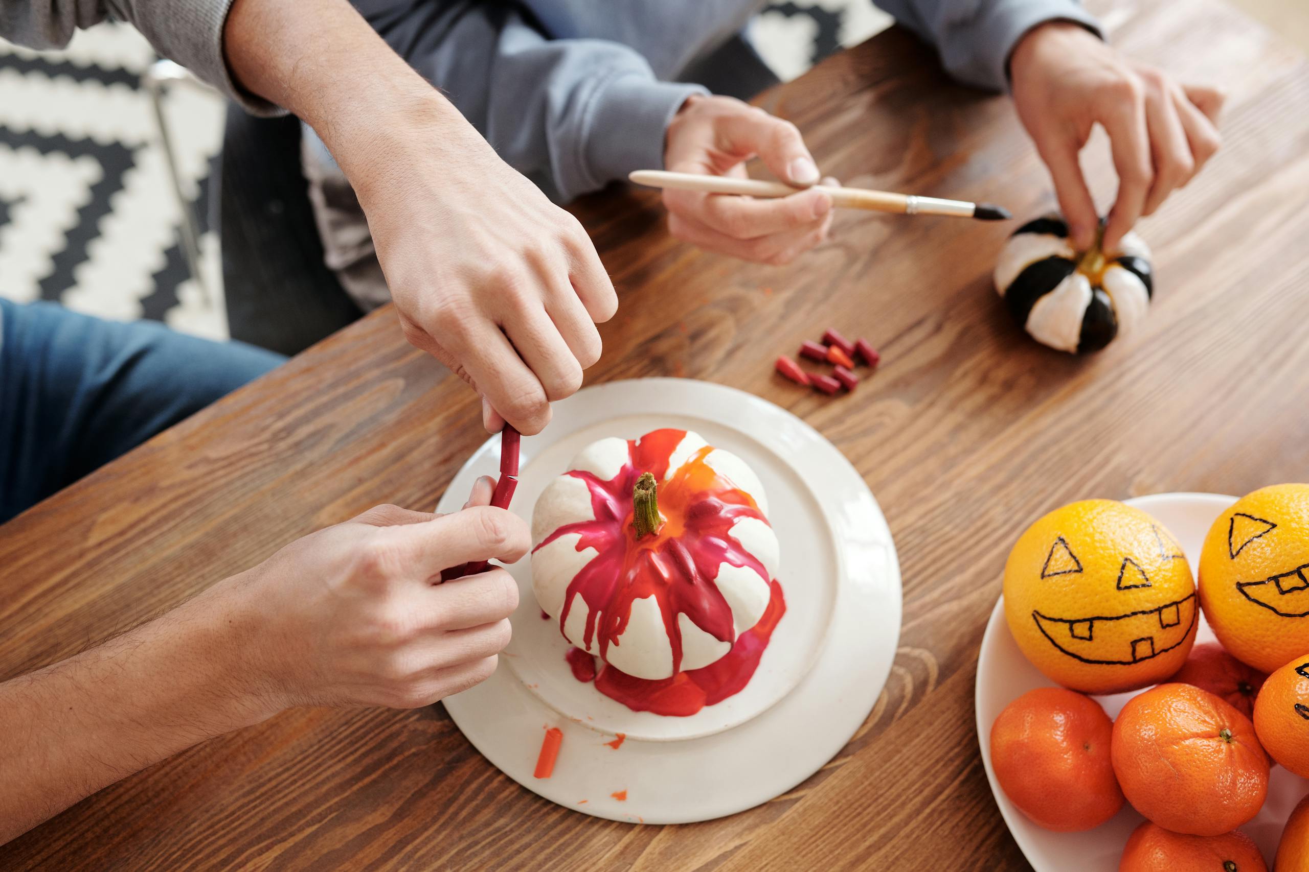 Adults painting pumpkins and oranges for Halloween with colorful designs. Indoor creative activity.