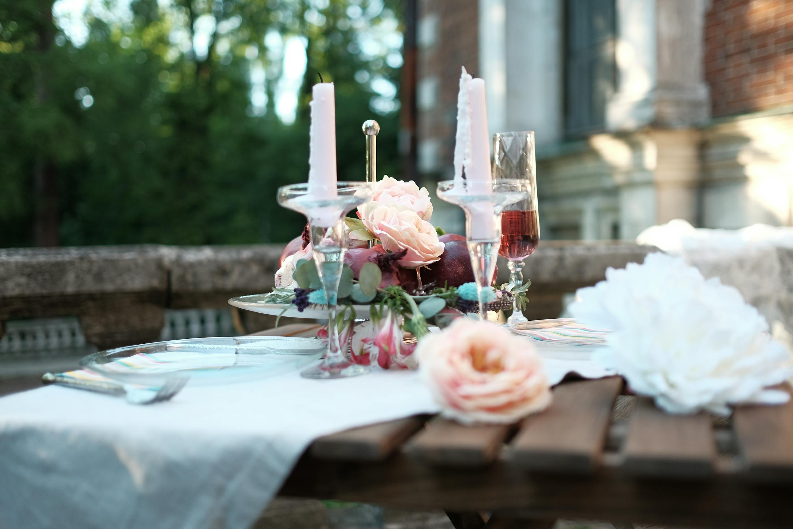 Charming outdoor table setting with pink roses, candles, and wine for a romantic occasion.