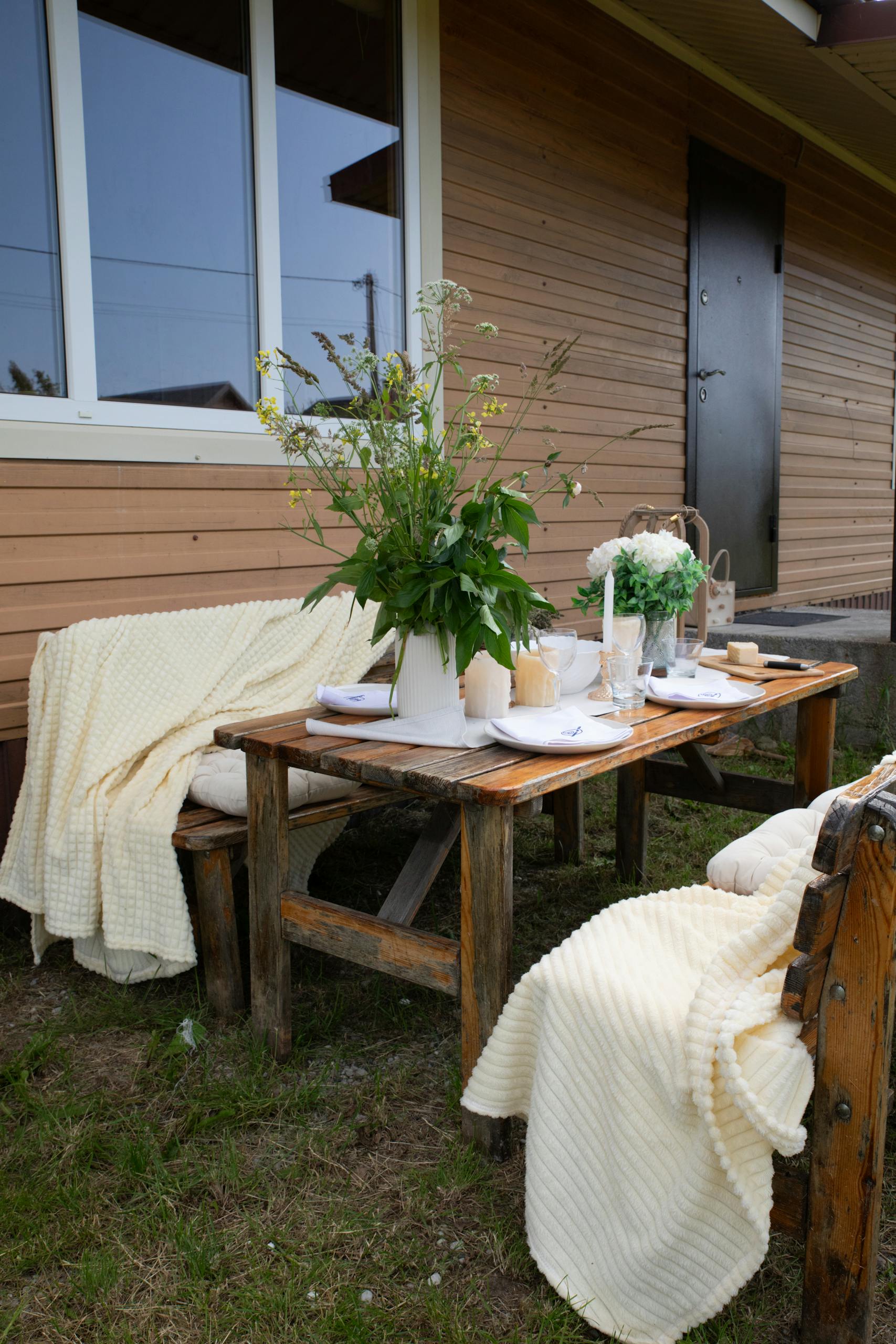 Charming rustic outdoor table setting with flowers and cozy blankets, perfect for a summer gathering.