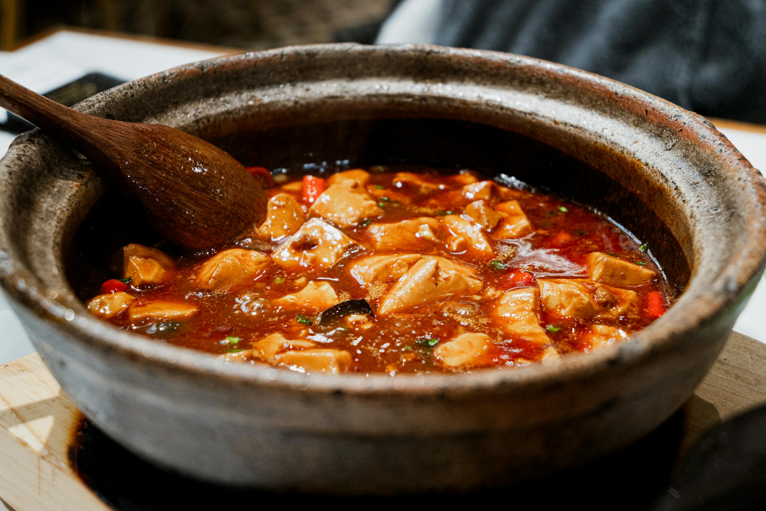 Close-up of a flavourful stew simmering in a rustic pot with a wooden spoon.
