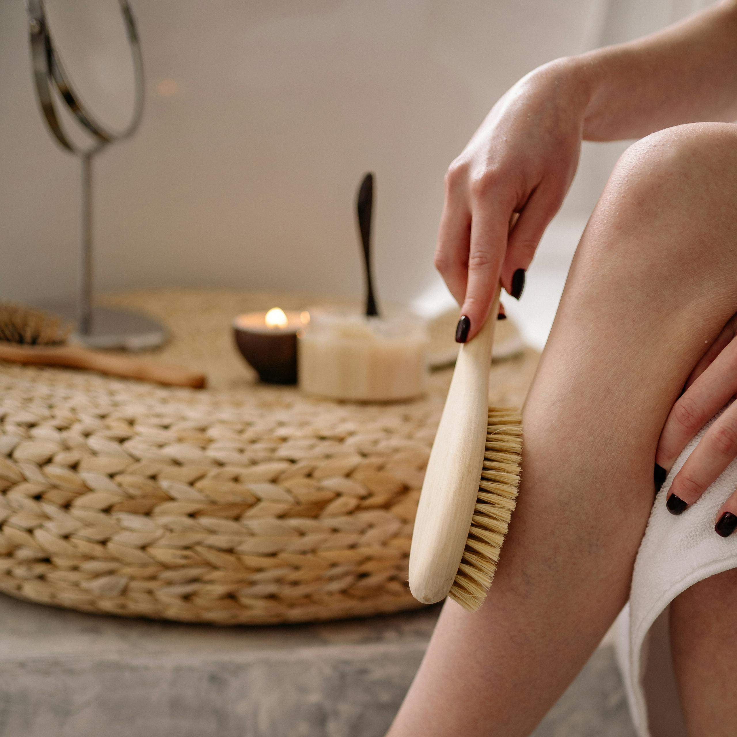 Close-up of a woman using a dry brush for skin exfoliation in a cozy bathroom setting.