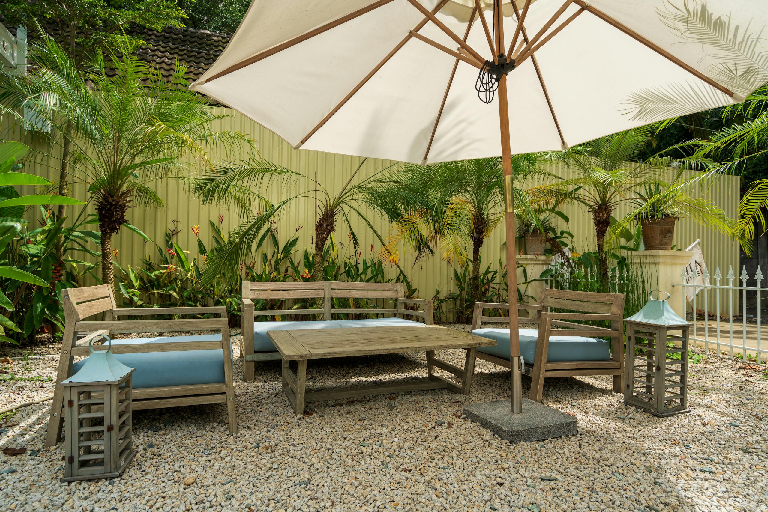 Cozy garden patio with wooden chairs, table, and umbrella surrounded by lush greenery.