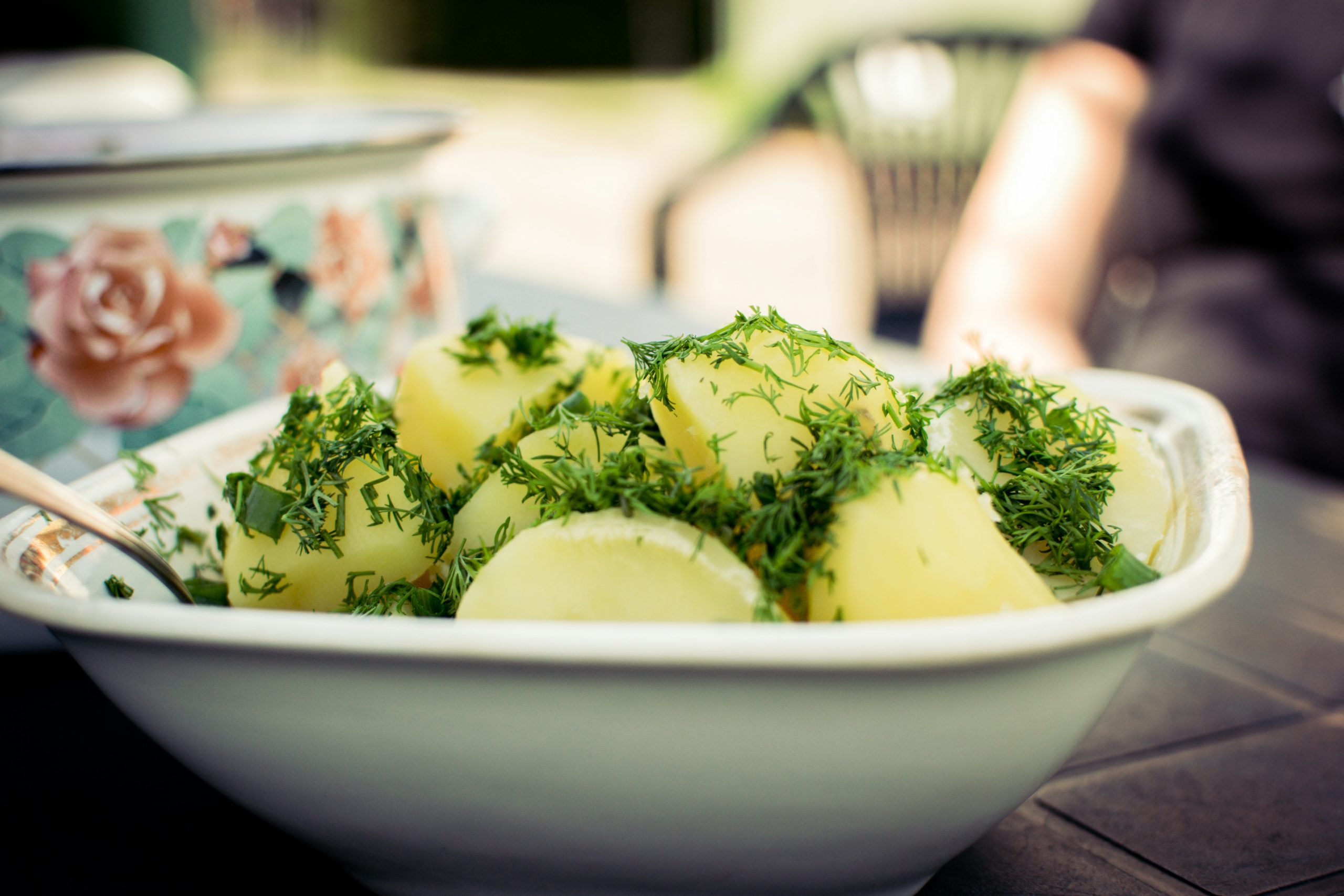 A large bowl of new potato salad tossed with fresh herbs, served in a white ceramic bowl