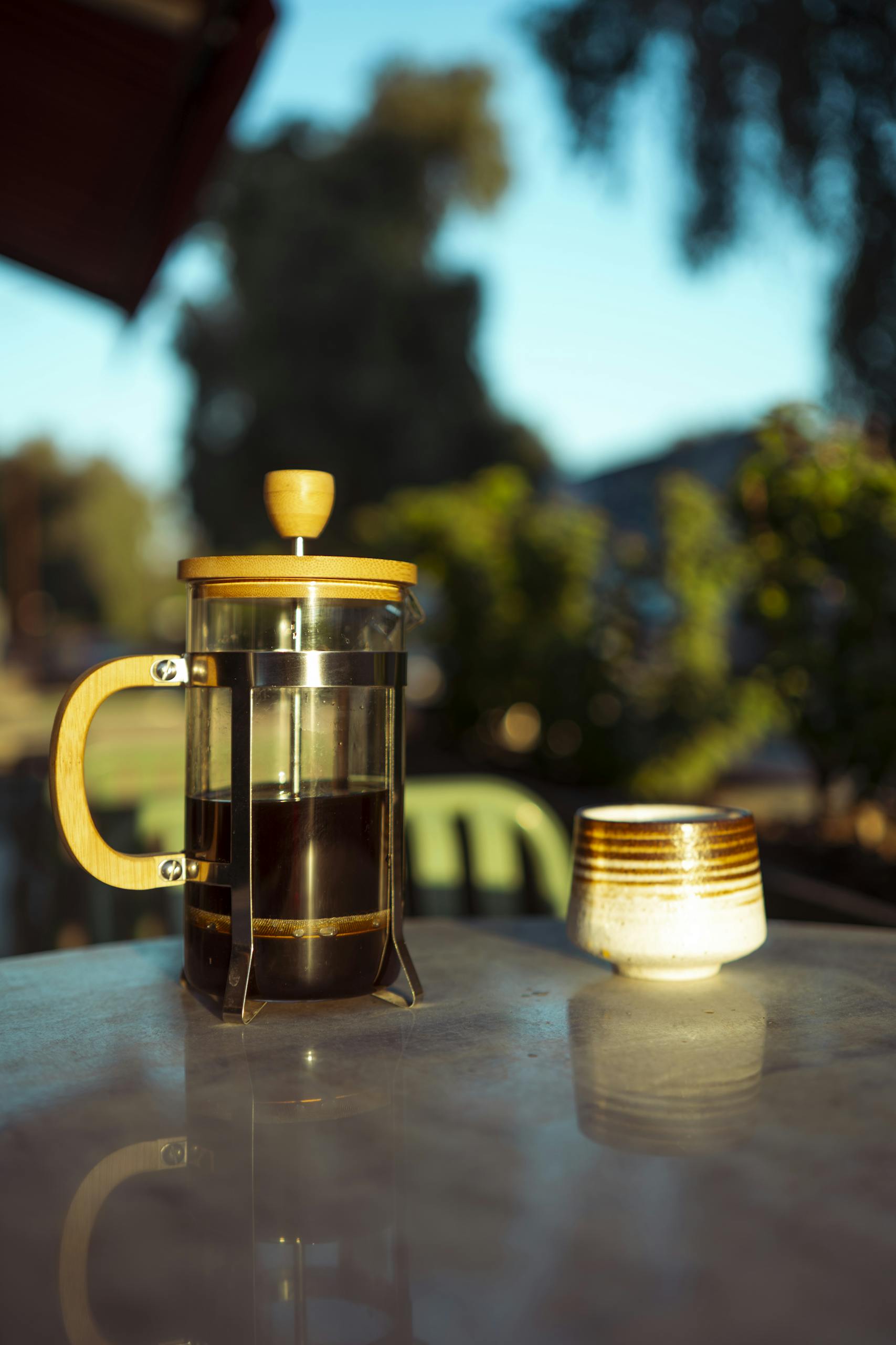 Elegant French press and mug on a sunlit table in an outdoor setting.
