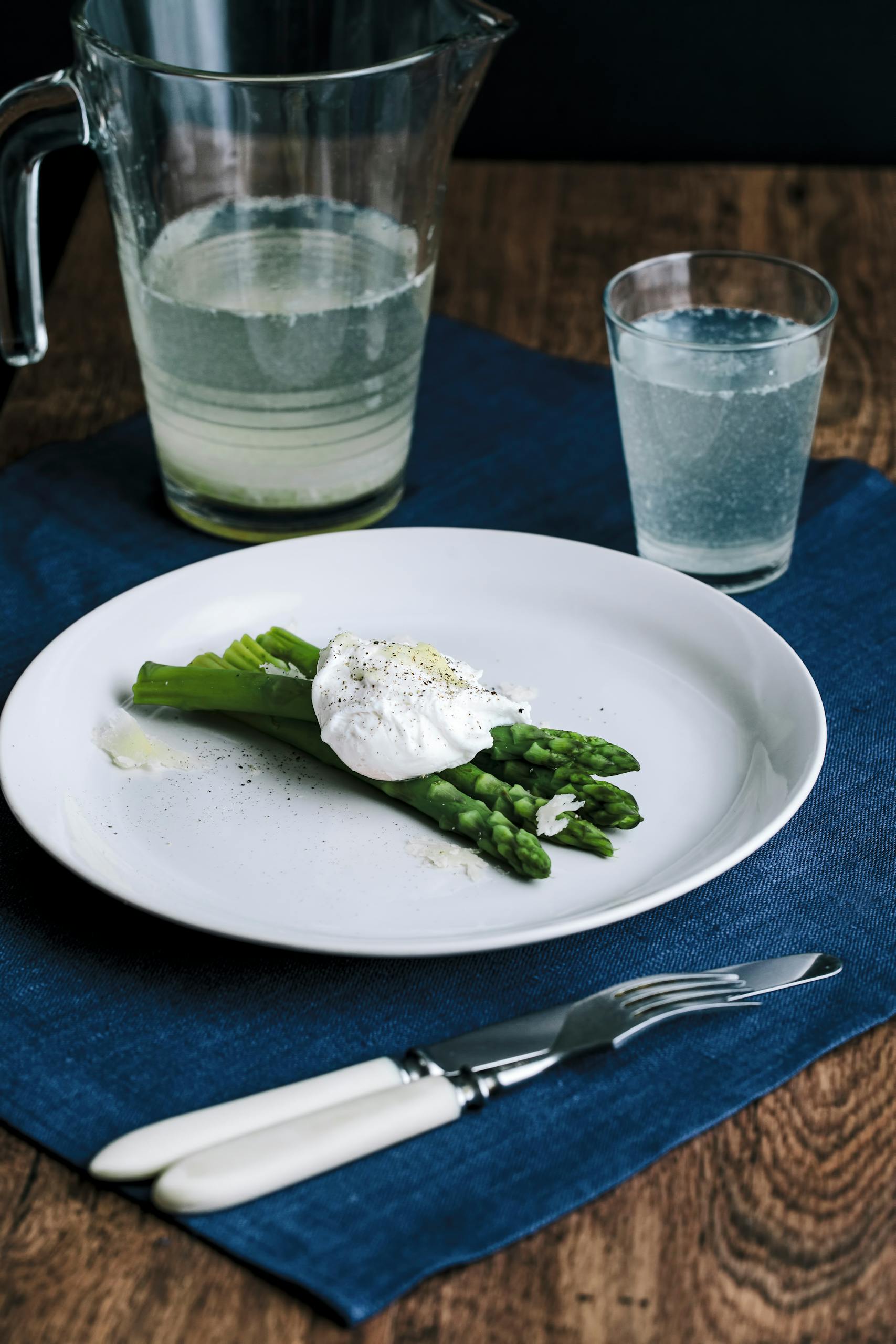 Elegant meal with poached egg on asparagus, complemented by a refreshing drink.