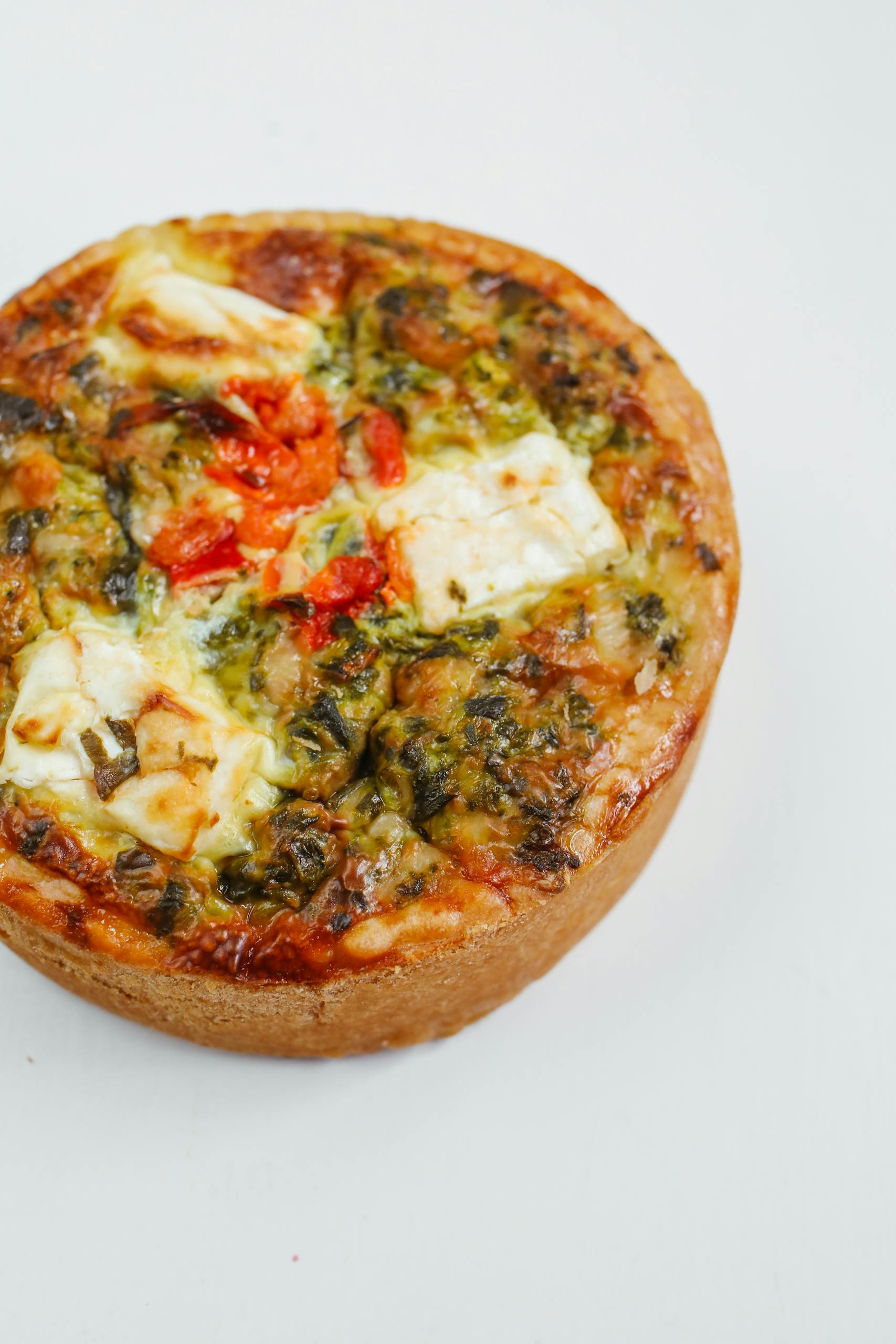 Freshly baked spinach and cheese quiche on a clean white background.