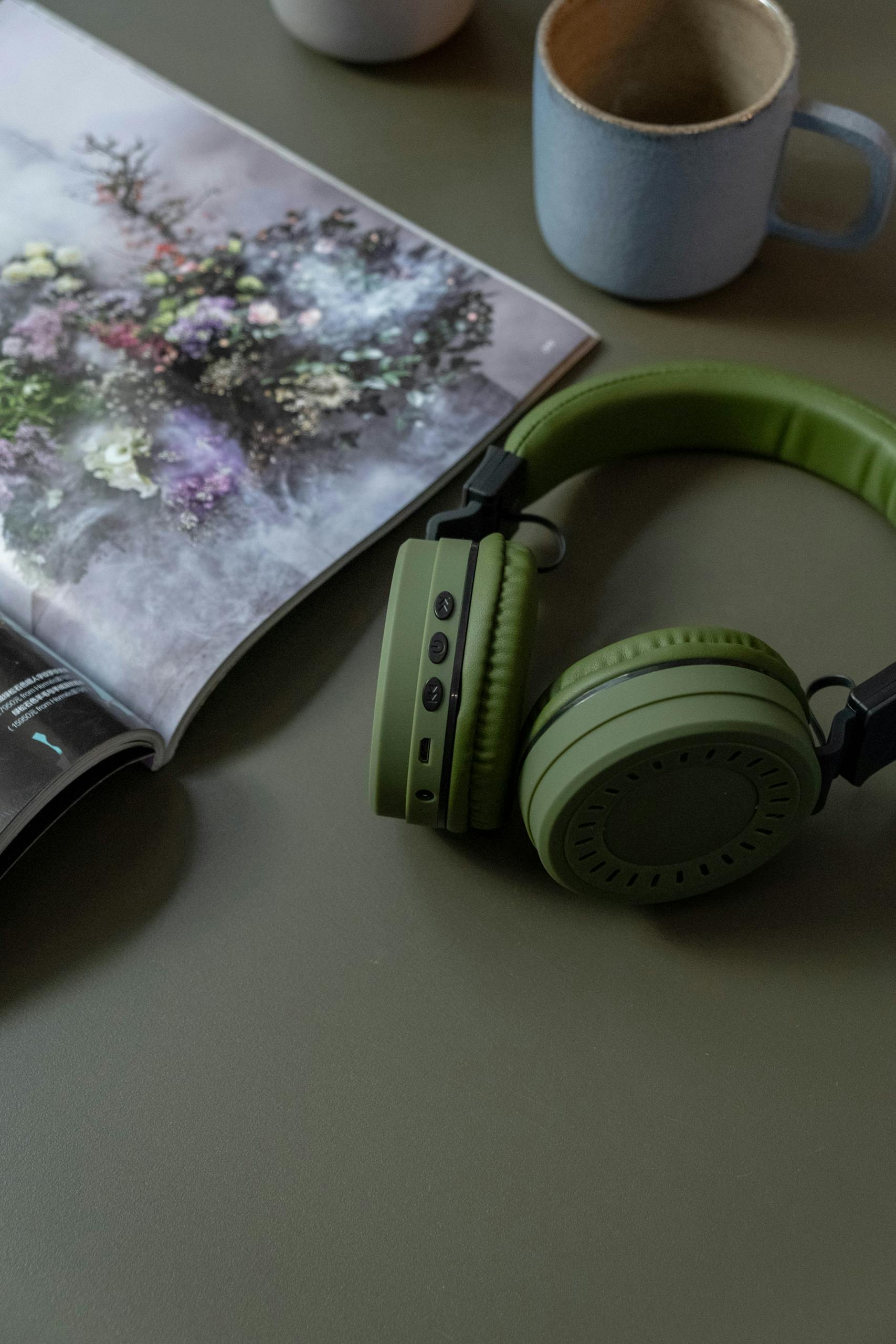 Green headphones and magazine on a table with a mug, creating a casual mood.